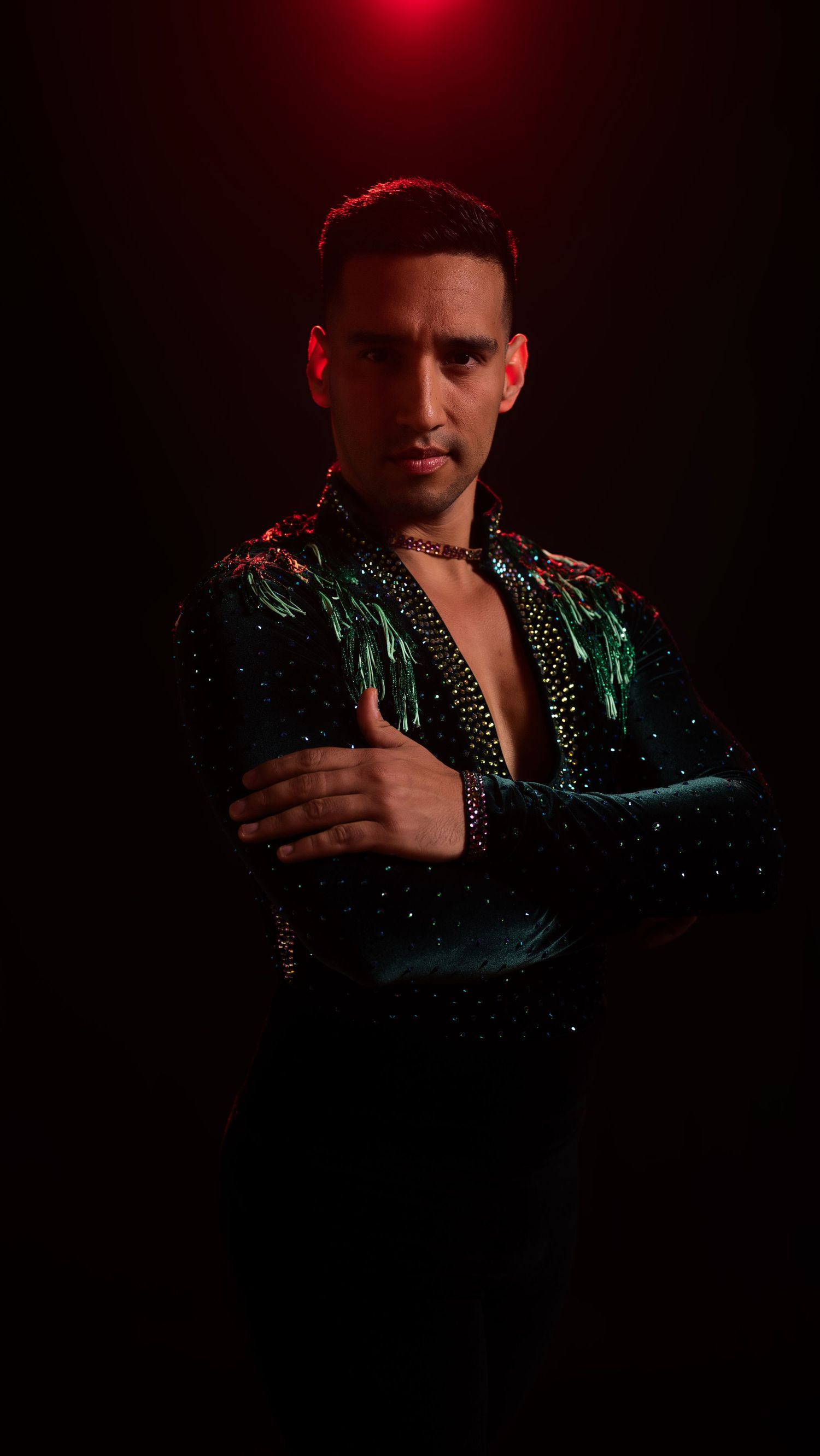 Dramatic portrait of a dancer in a sparkling green jacket under red lighting against a dark background.