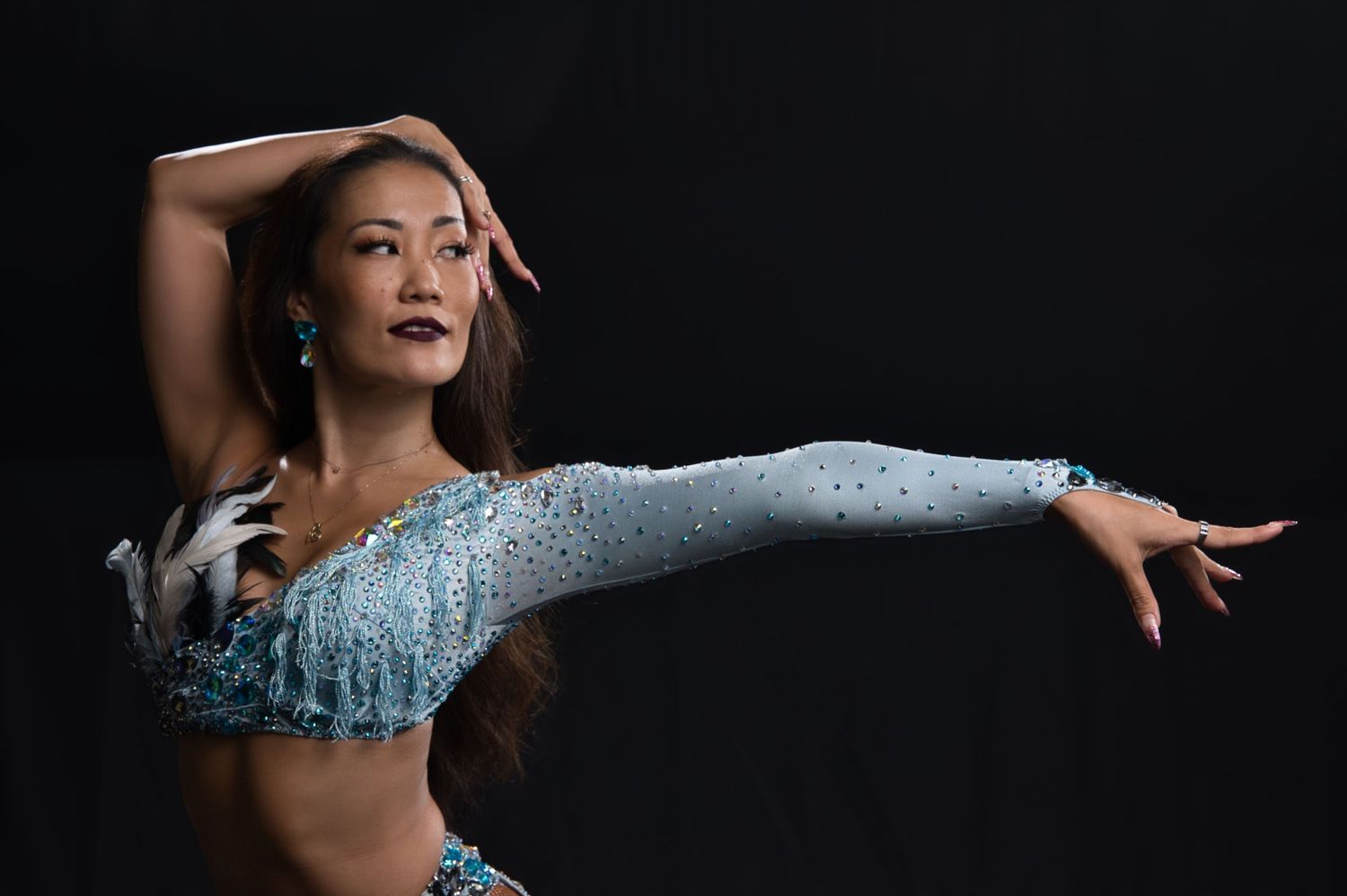 Dancer in sparkling blue costume performs expressive arm movement during studio shoot.
