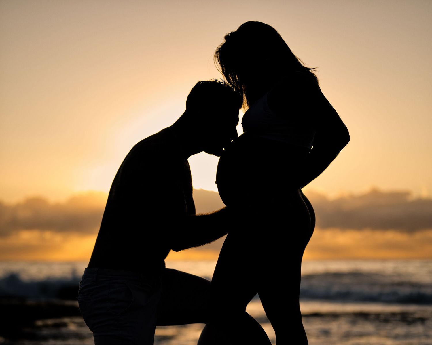Silhouette of a couple embracing on the beach during golden hour sunset.