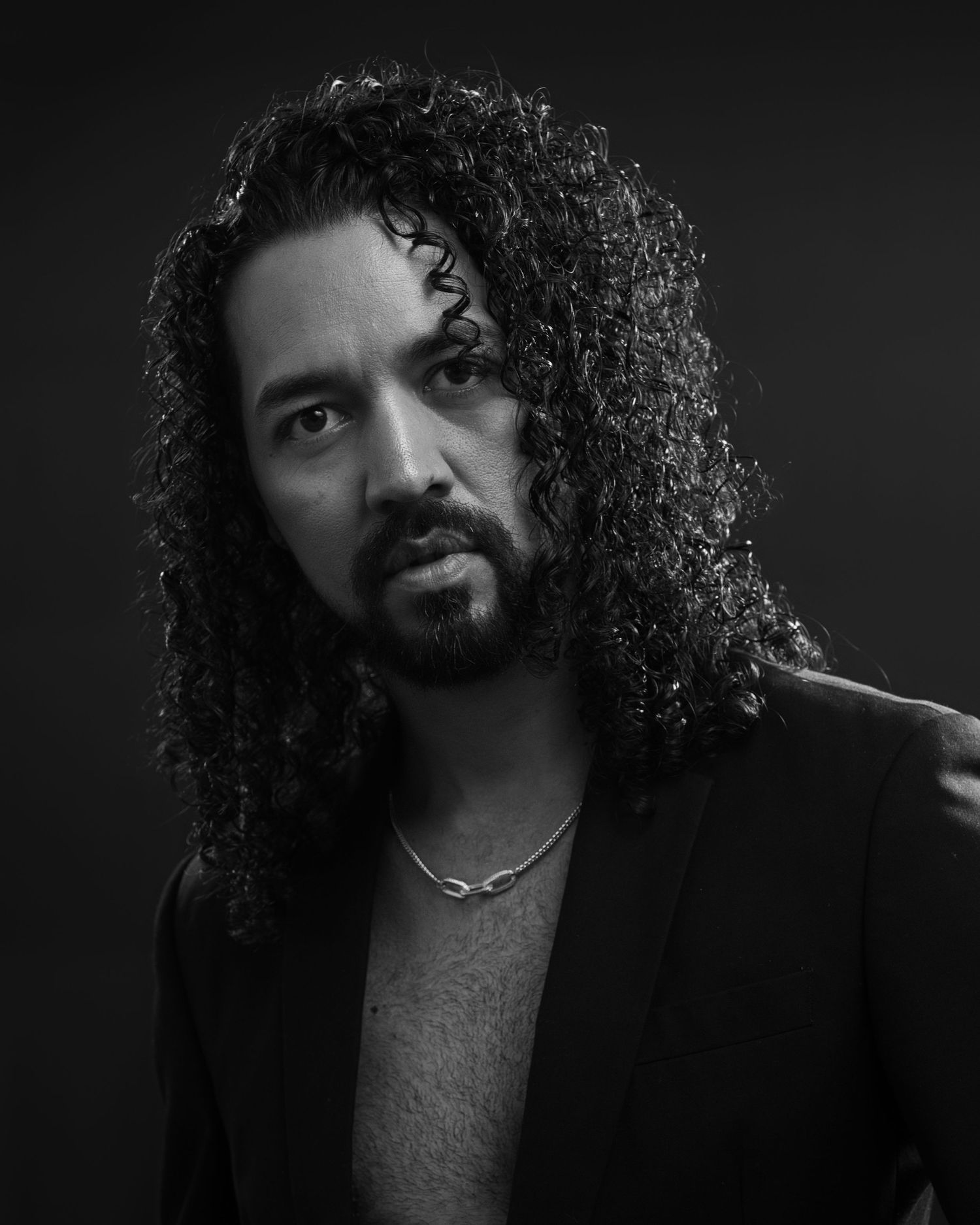 Black and white portrait of a person with long curly hair wearing a dark blazer.