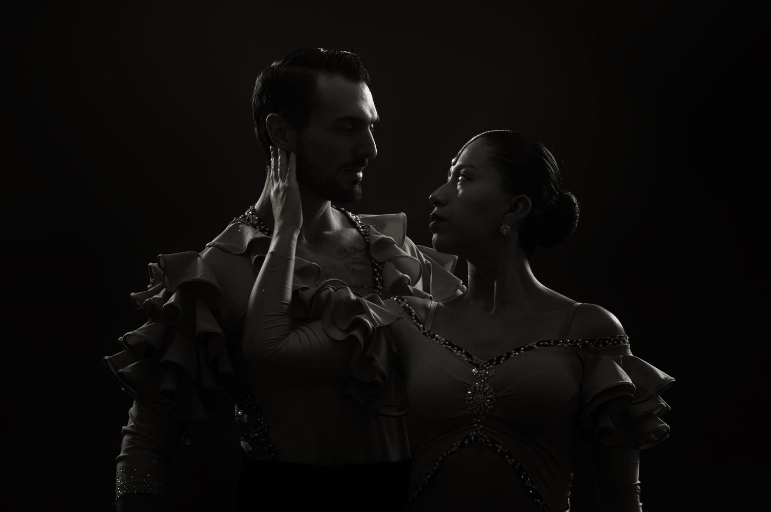 Dramatic black and white portrait of couple in elegant dance pose with atmospheric lighting.