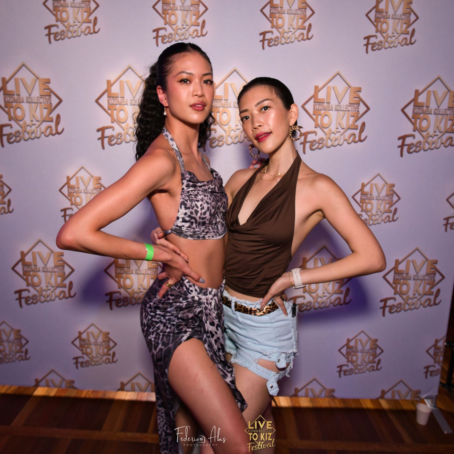 Two dancers posing against branded backdrop at dance event.