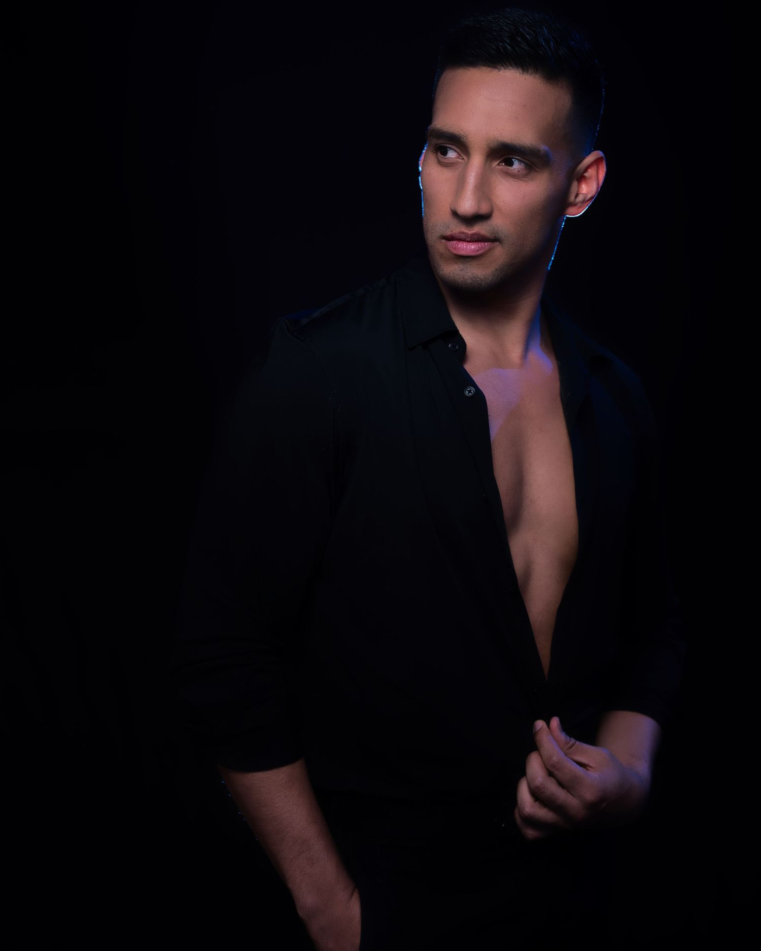 Moody studio portrait showing figure in open black jacket against dark background.