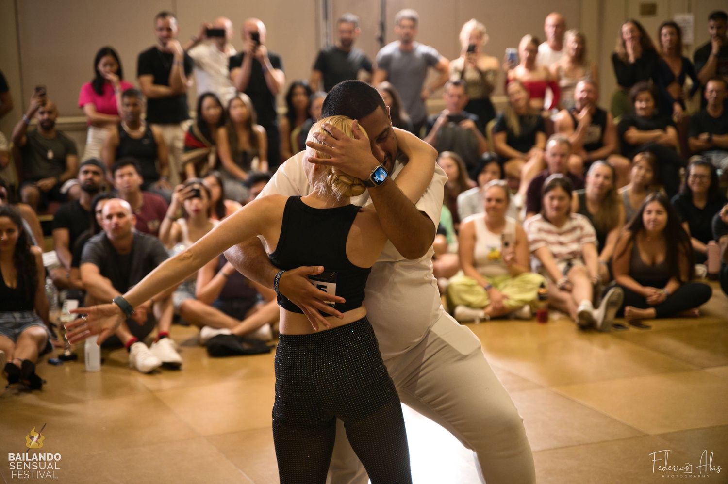 Dancers performing an energetic dance move at a social dance event with crowd in background.