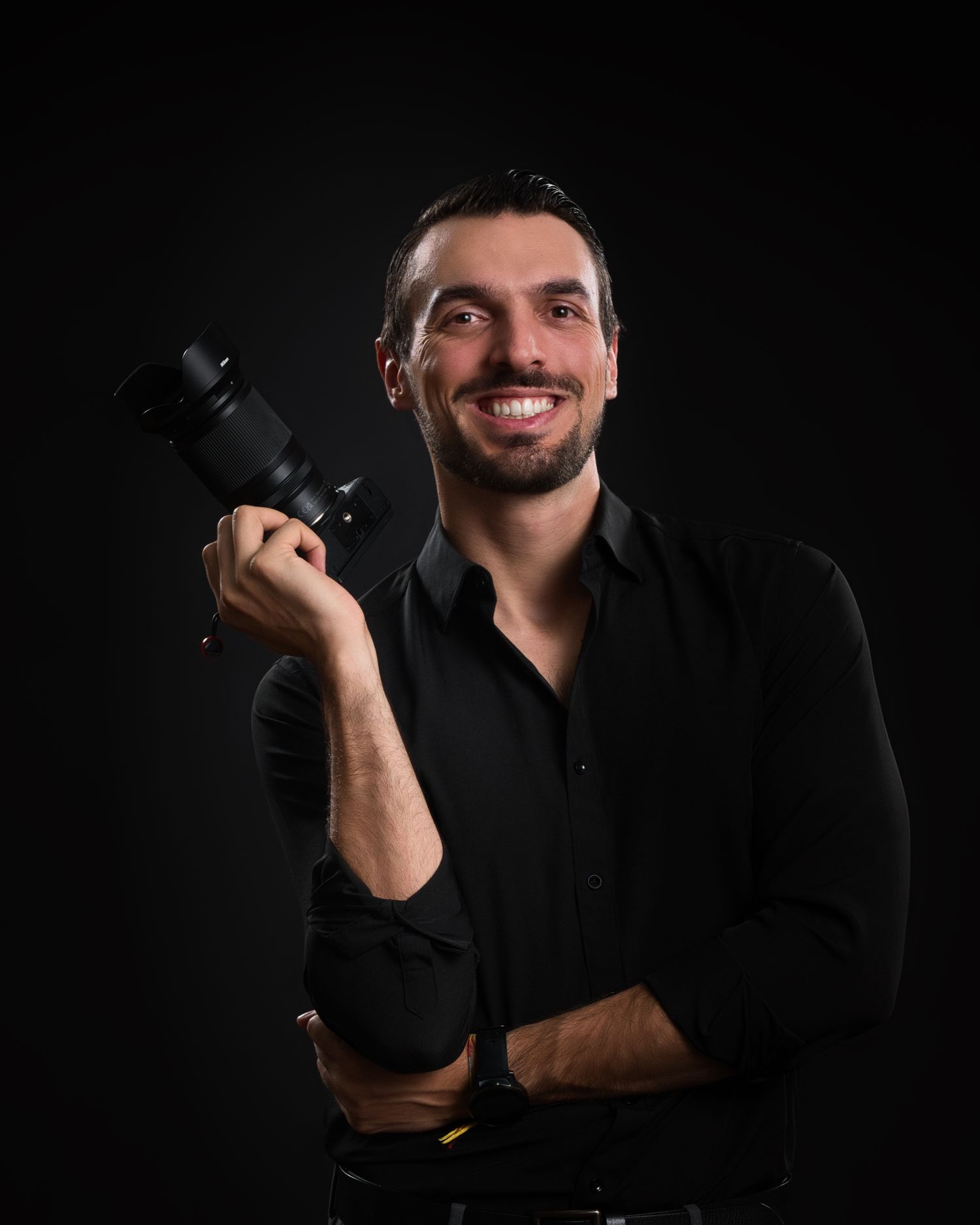 Professional photographer in black shirt holding camera against dark background.