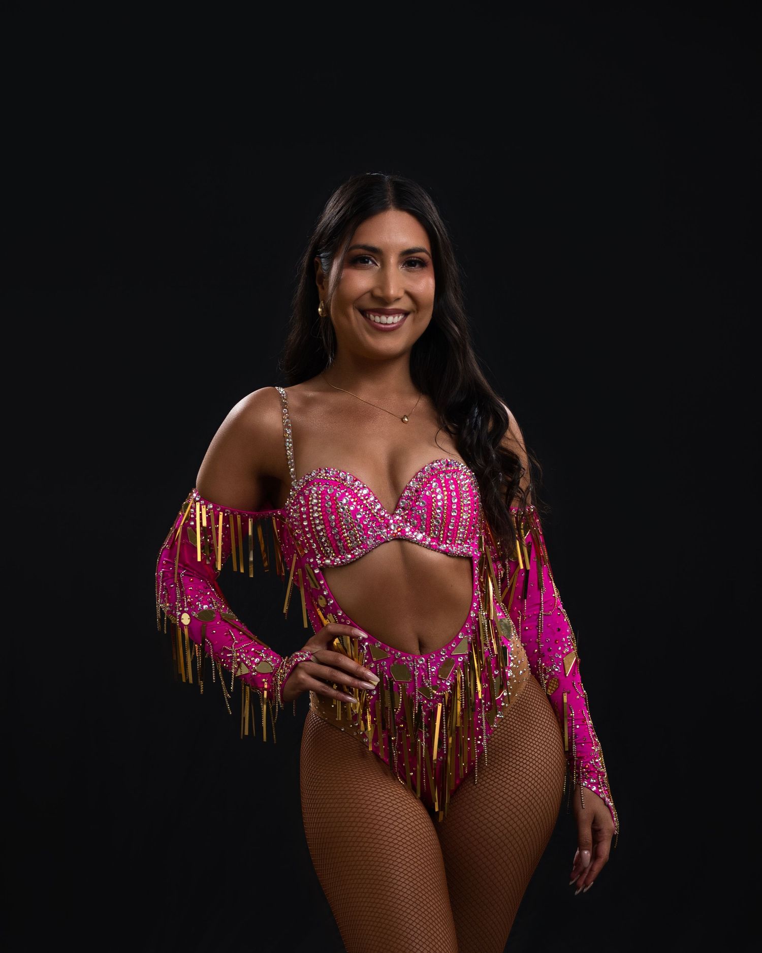 Dancer in sparkling pink and gold fringe performance costume posing against dark background.