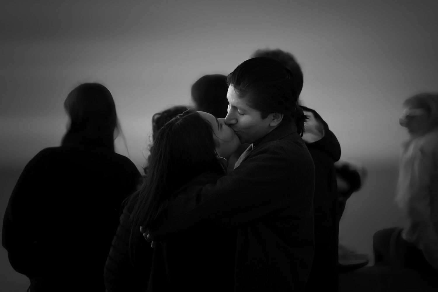 Silhouetted couples embrace while watching sunset in moody black and white photograph.