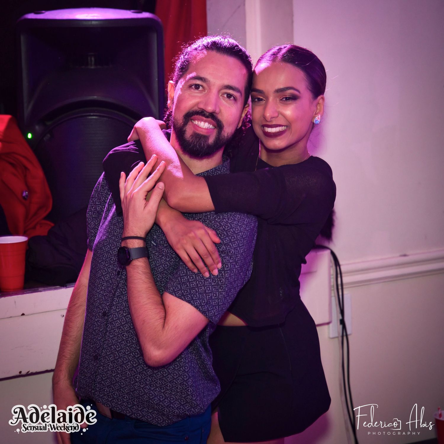 Two people sharing an embrace while dancing at a nightclub with purple lighting.