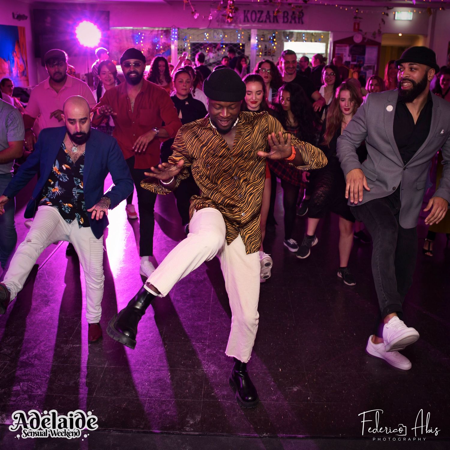 Dancers showing off their moves on a crowded dance floor under purple lights.