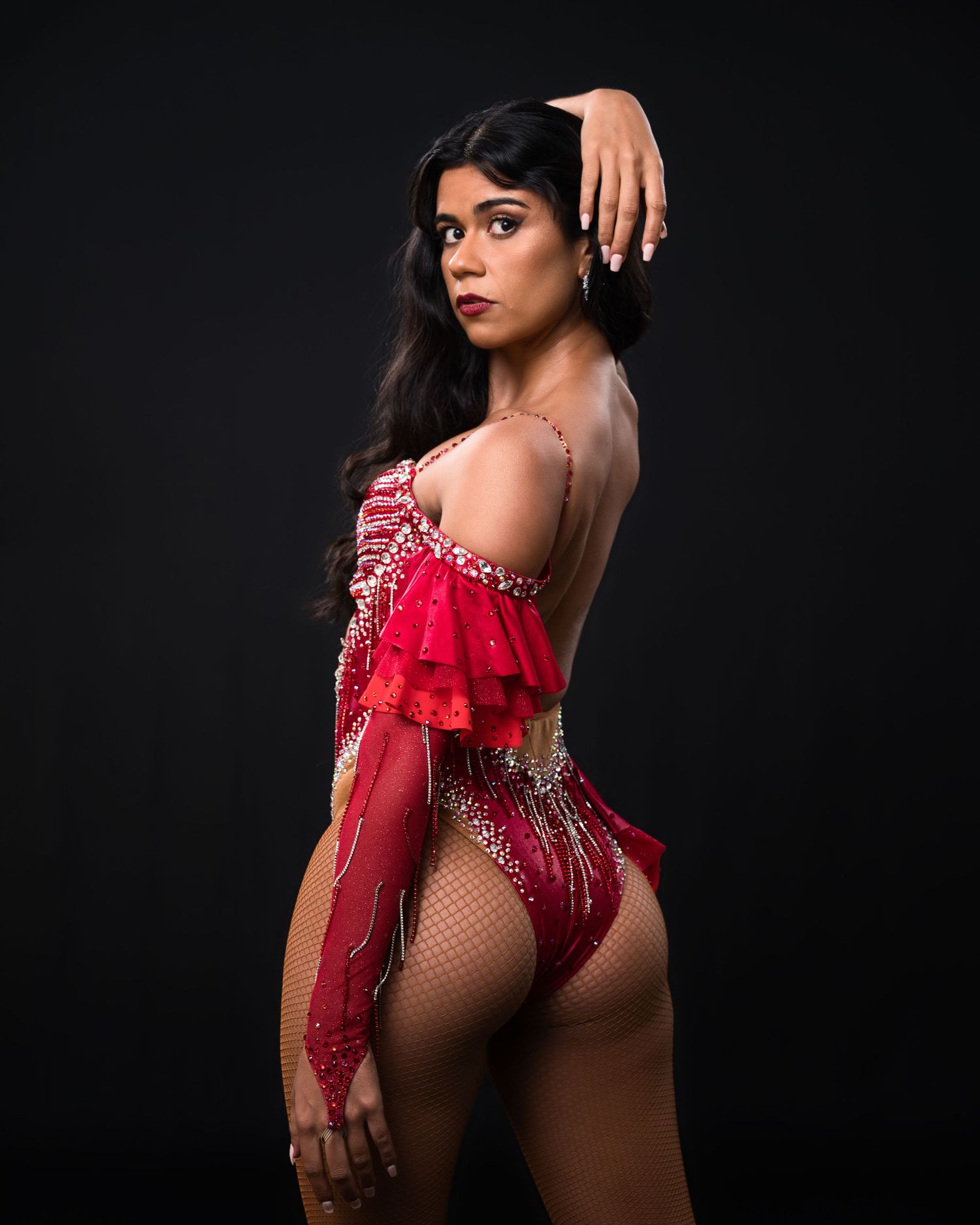 Dancer in red embellished performance costume poses against dark background.