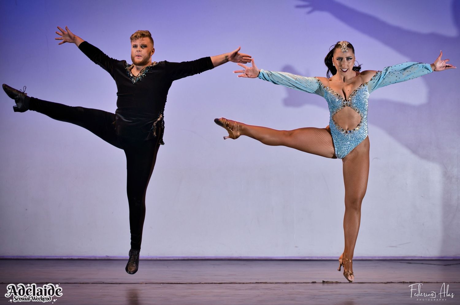 Two performers executing synchronized jumps in dance costumes on stage.