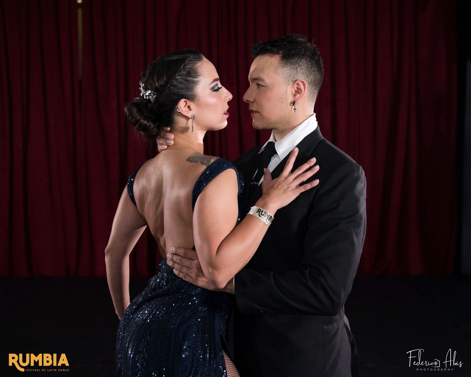 A romantic dance pose in formal attire against a red curtain backdrop at a dance performance.