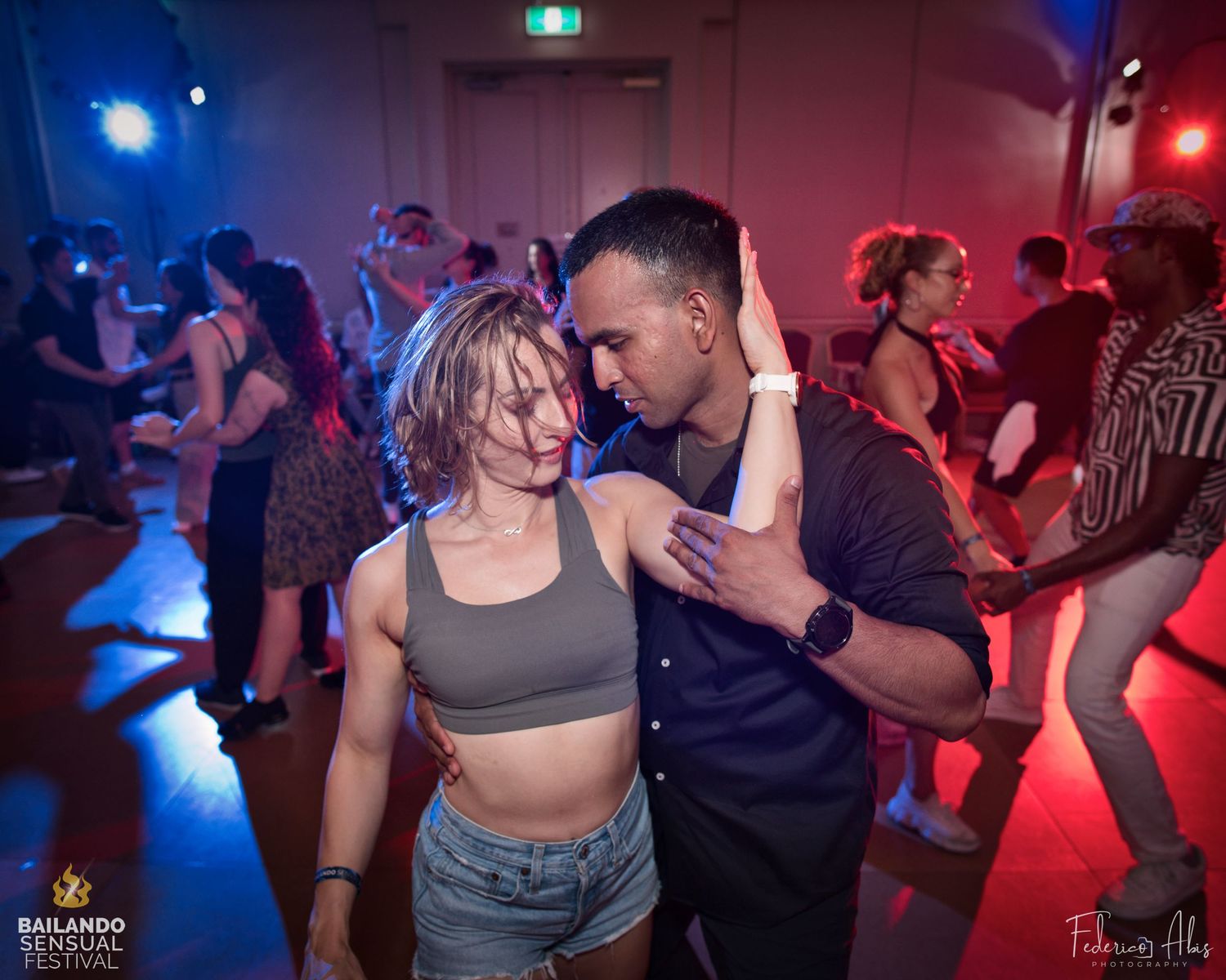 Dancers moving together on a dance floor illuminated by red and blue lights.