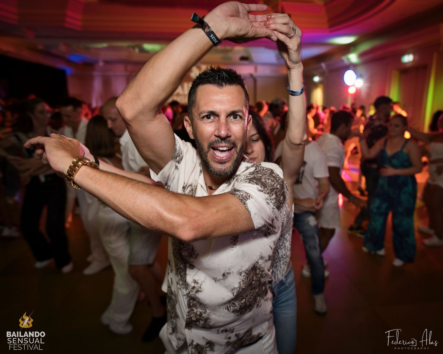 Energetic dancer in white shirt performing enthusiastic dance moves under colorful lights.