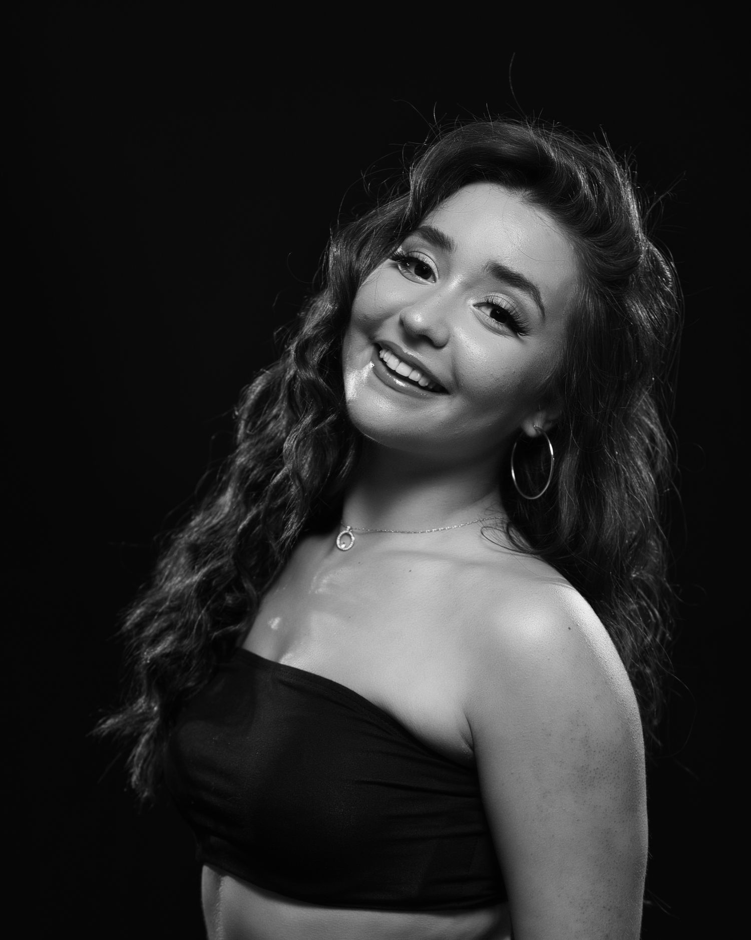 Black and white portrait of a smiling person in strapless top with long wavy hair.