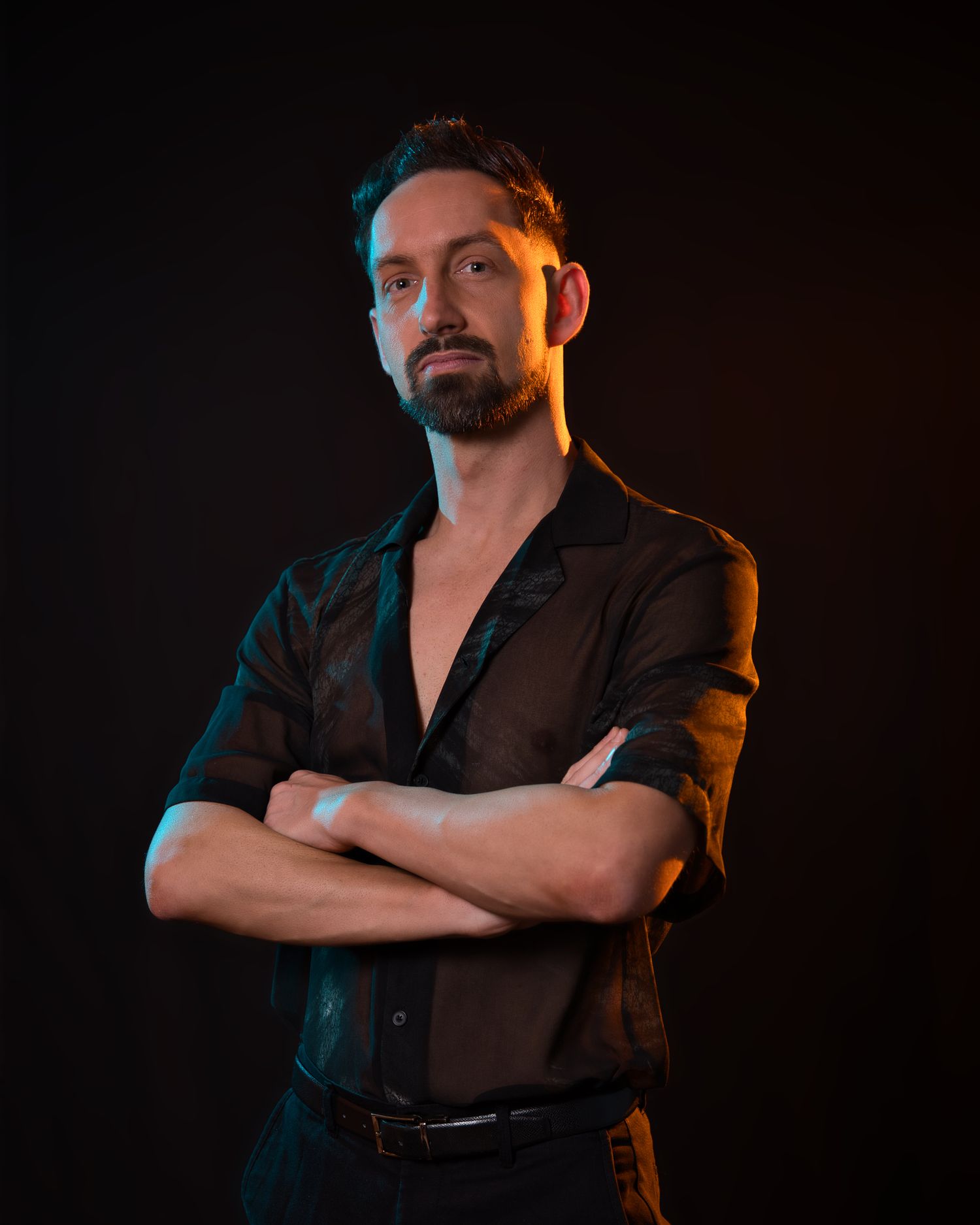 Moody portrait of person in black shirt against dark background with dramatic lighting.