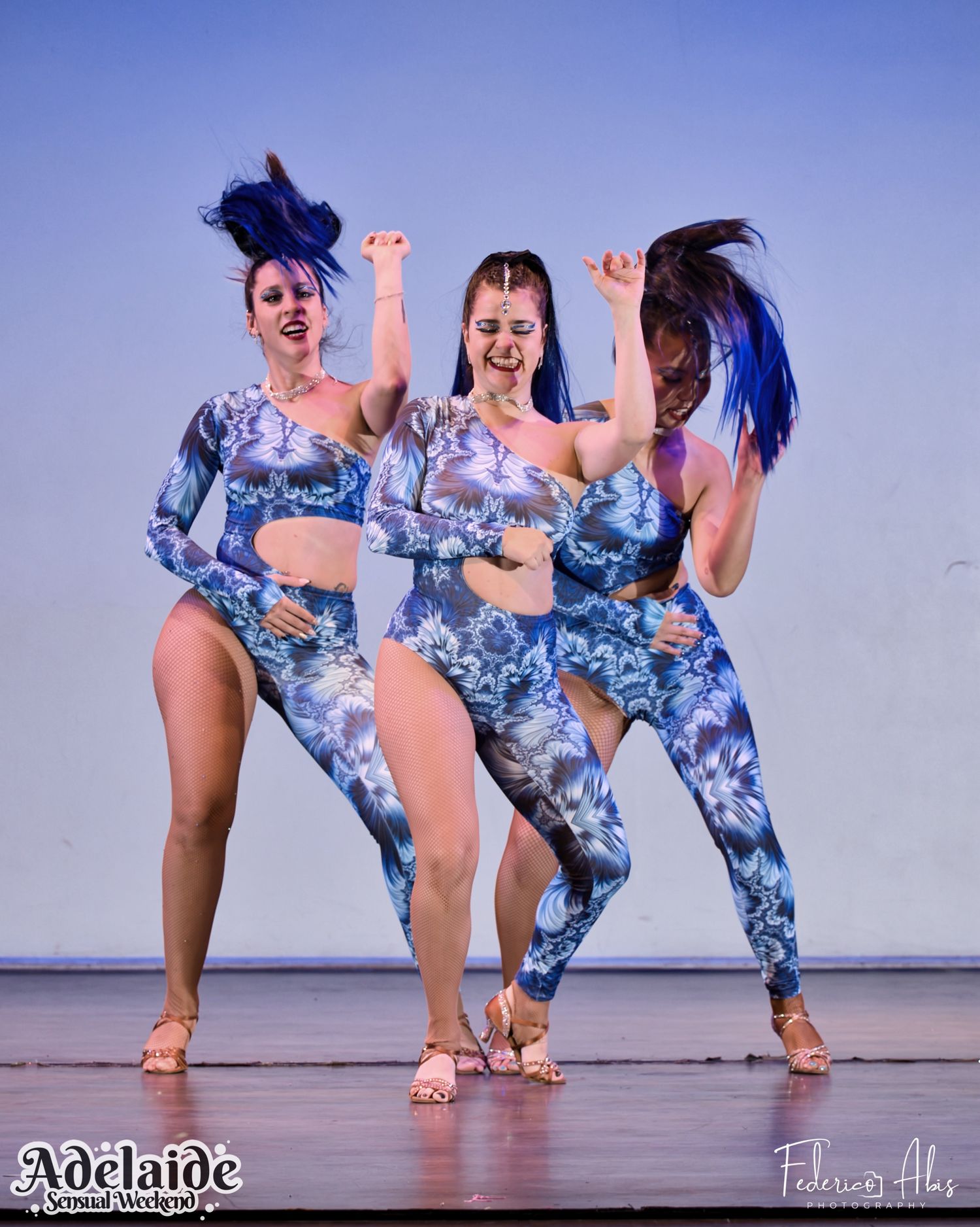 Three dancers in matching blue patterned outfits performing synchronized dance moves.