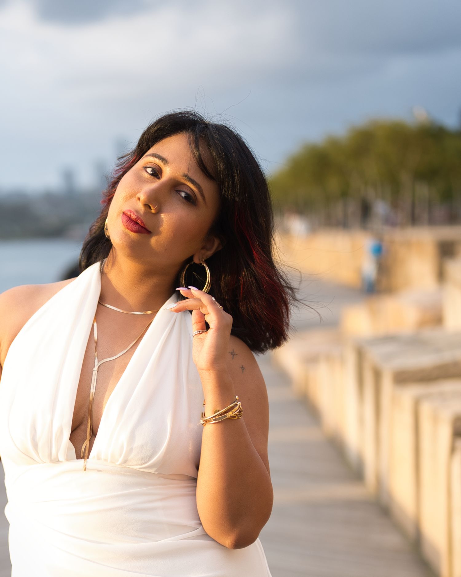 A woman in a white dress poses against a coastal backdrop with cloudy skies.