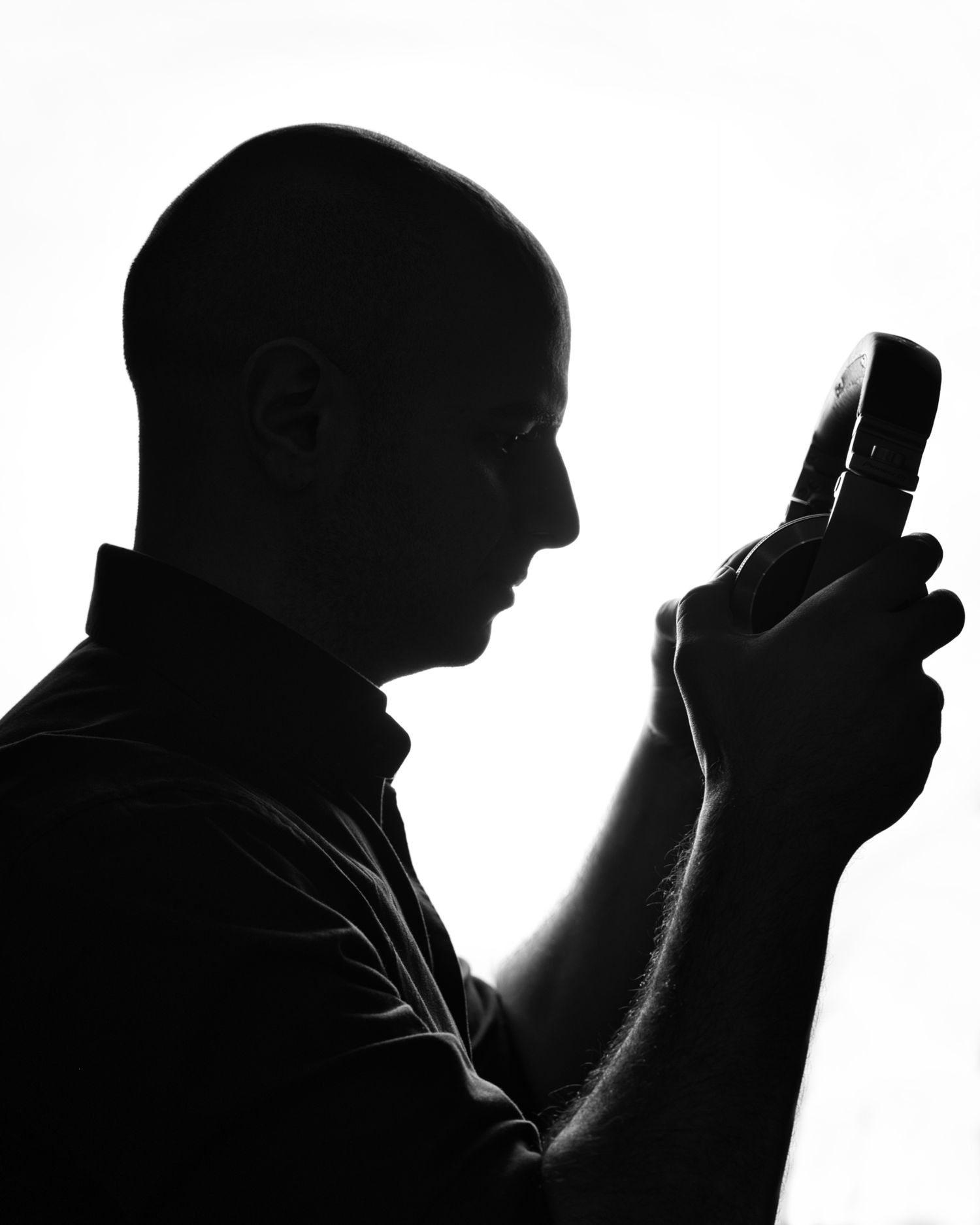 Dramatic silhouette portrait of a person holding a mobile phone against white background.