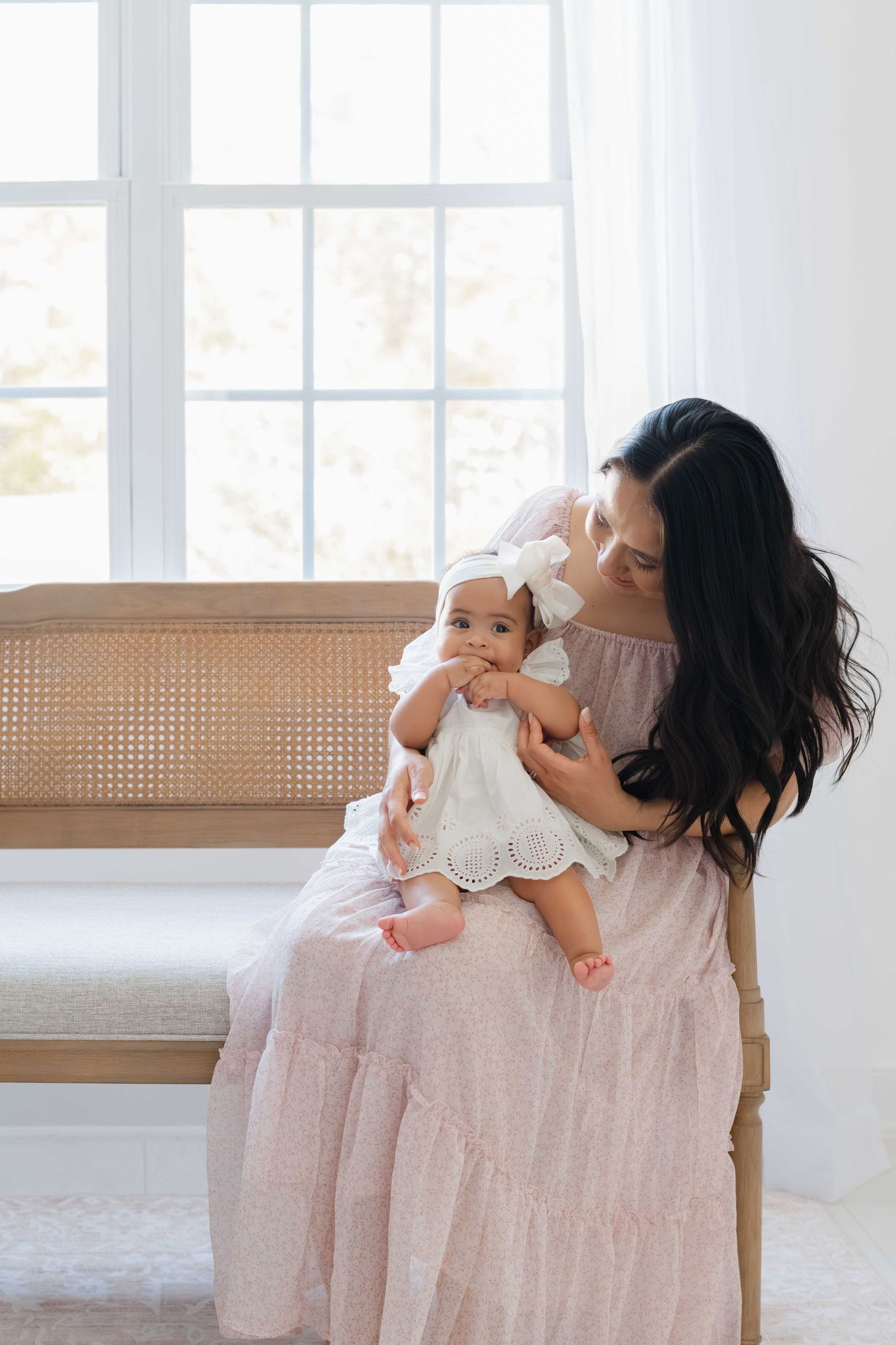 Mom in floral dress lovingly looks at her 8 month old baby in Richmond photography studio .