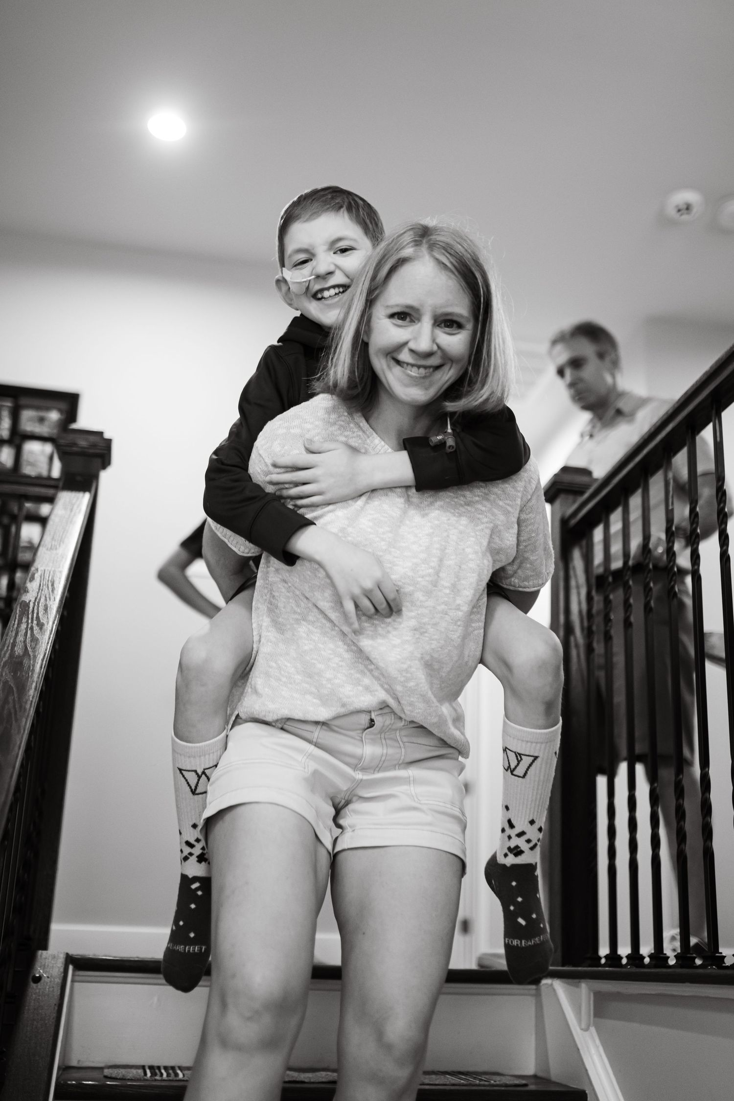 Woman giving piggyback ride to smiling boy on staircase in black and white family photo.