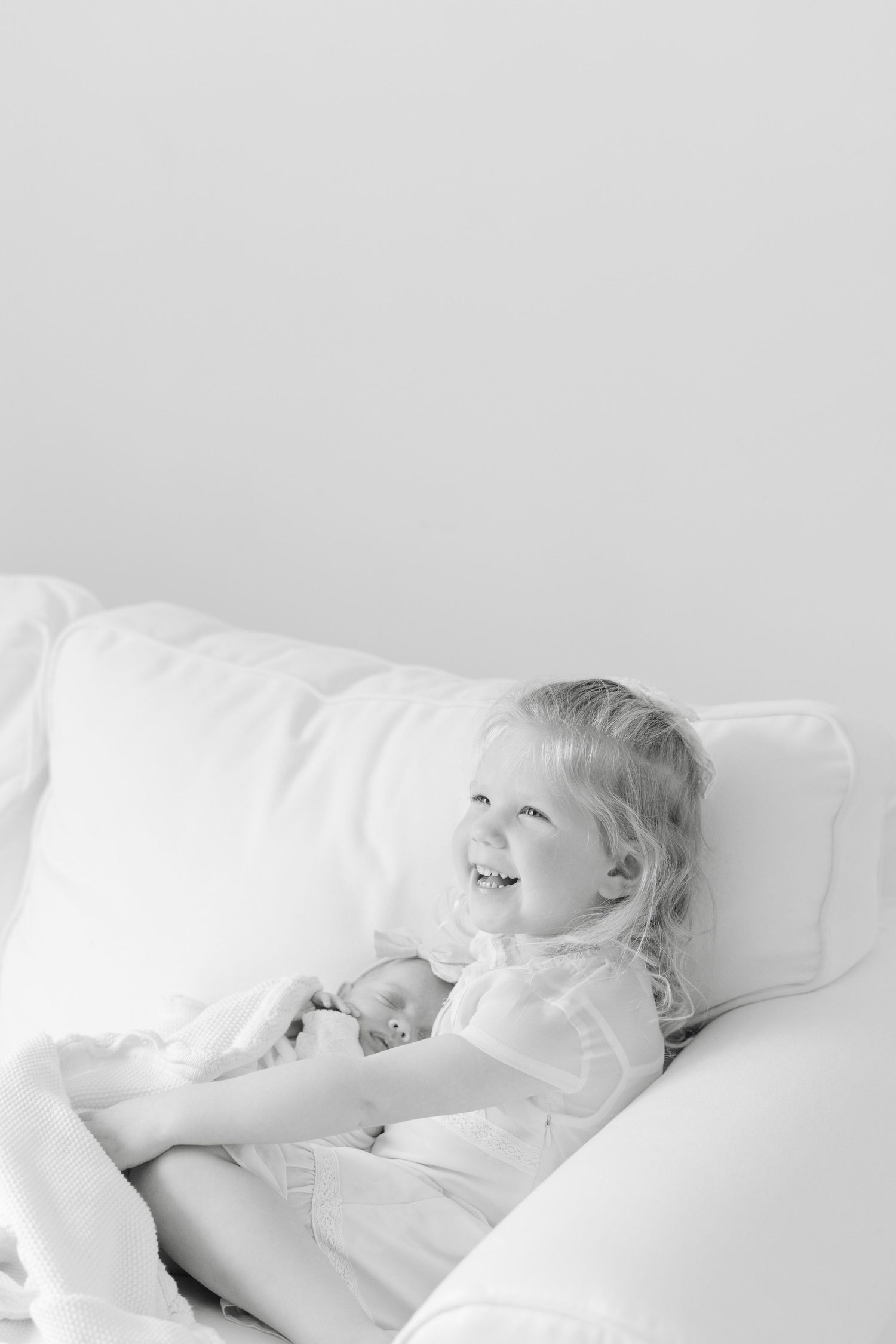 A sleeping child rests peacefully in white bedding while bathed in soft, natural light.