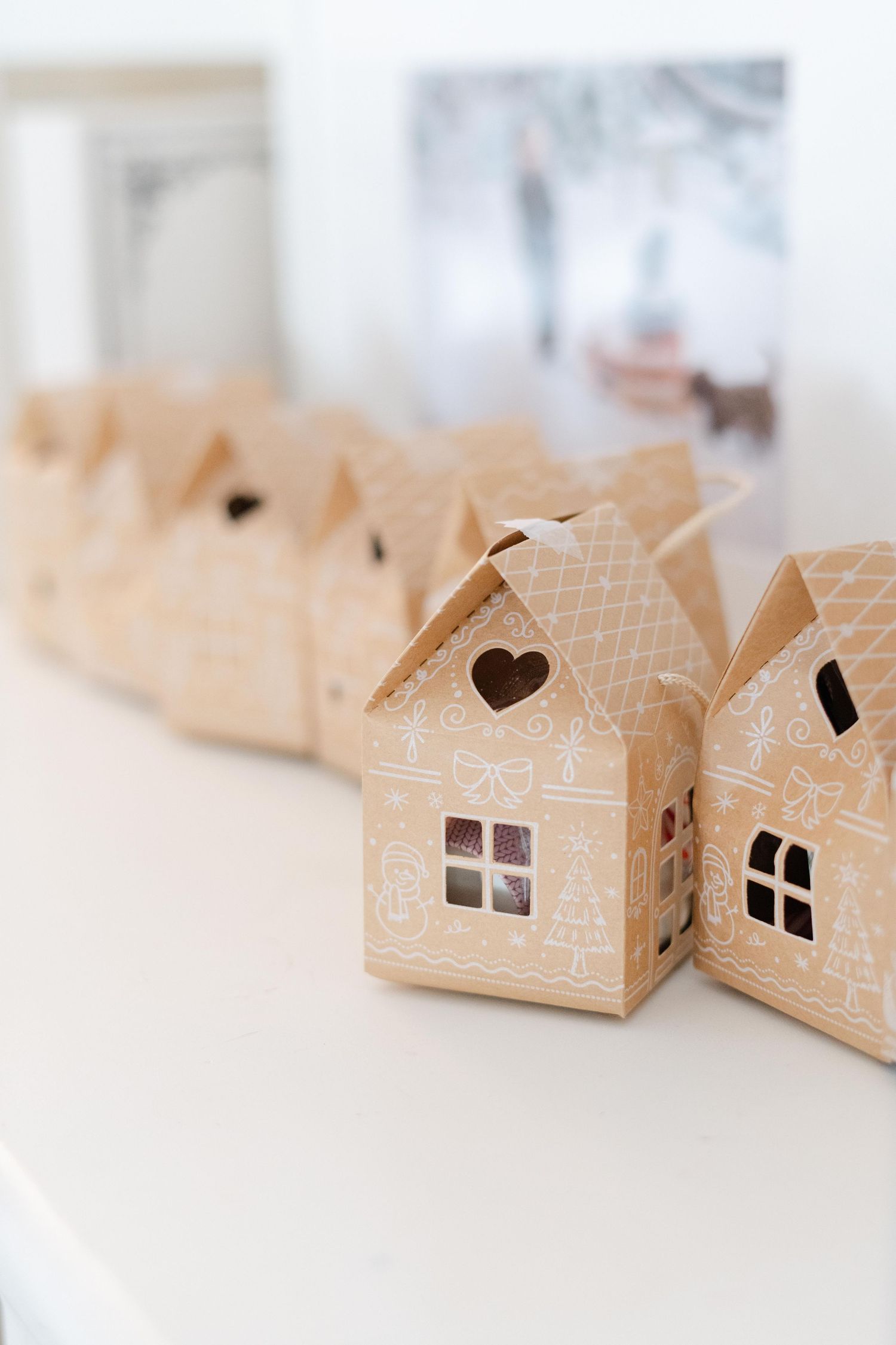 Kraft paper gingerbread house gift boxes with white decorative details lined up on a white surface.