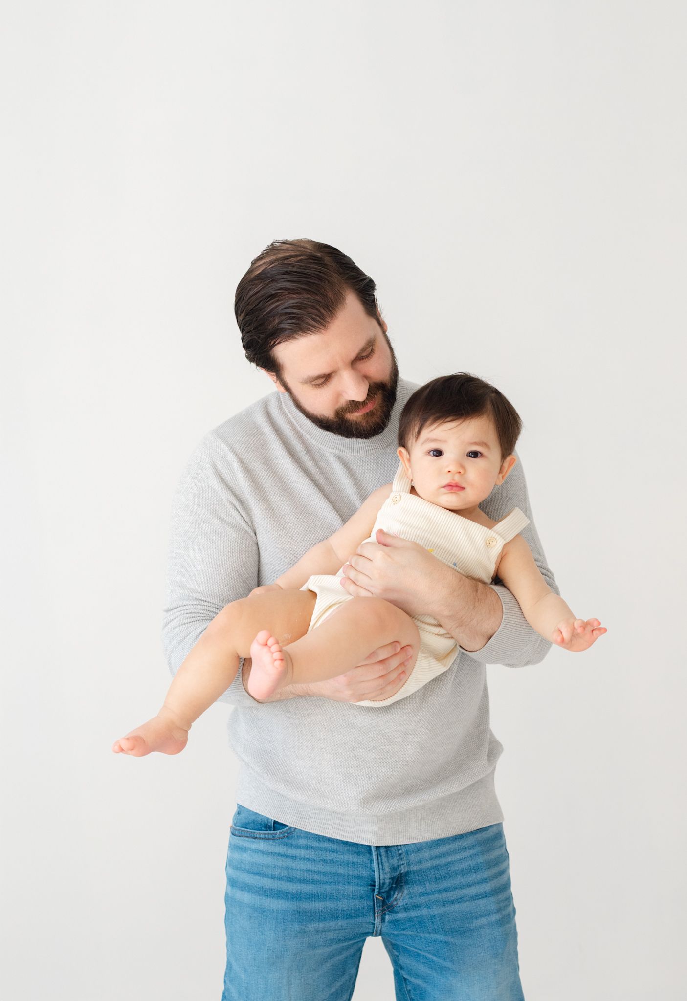 Parent holding baby in grey sweater against white background.