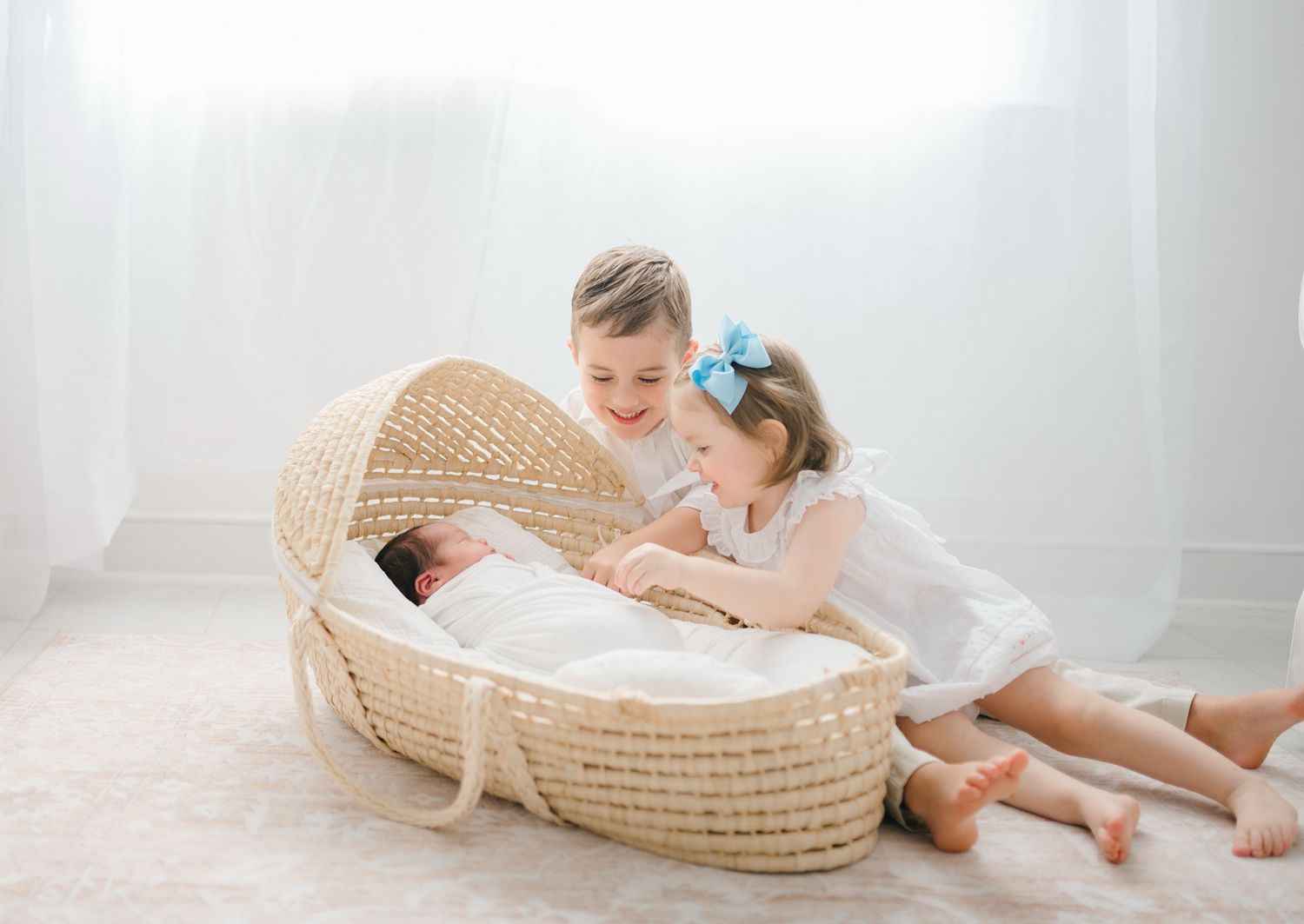 A baby lies peacefully in a woven moses basket on white bedding while wearing light colored clothing in Richmond newborn photographer