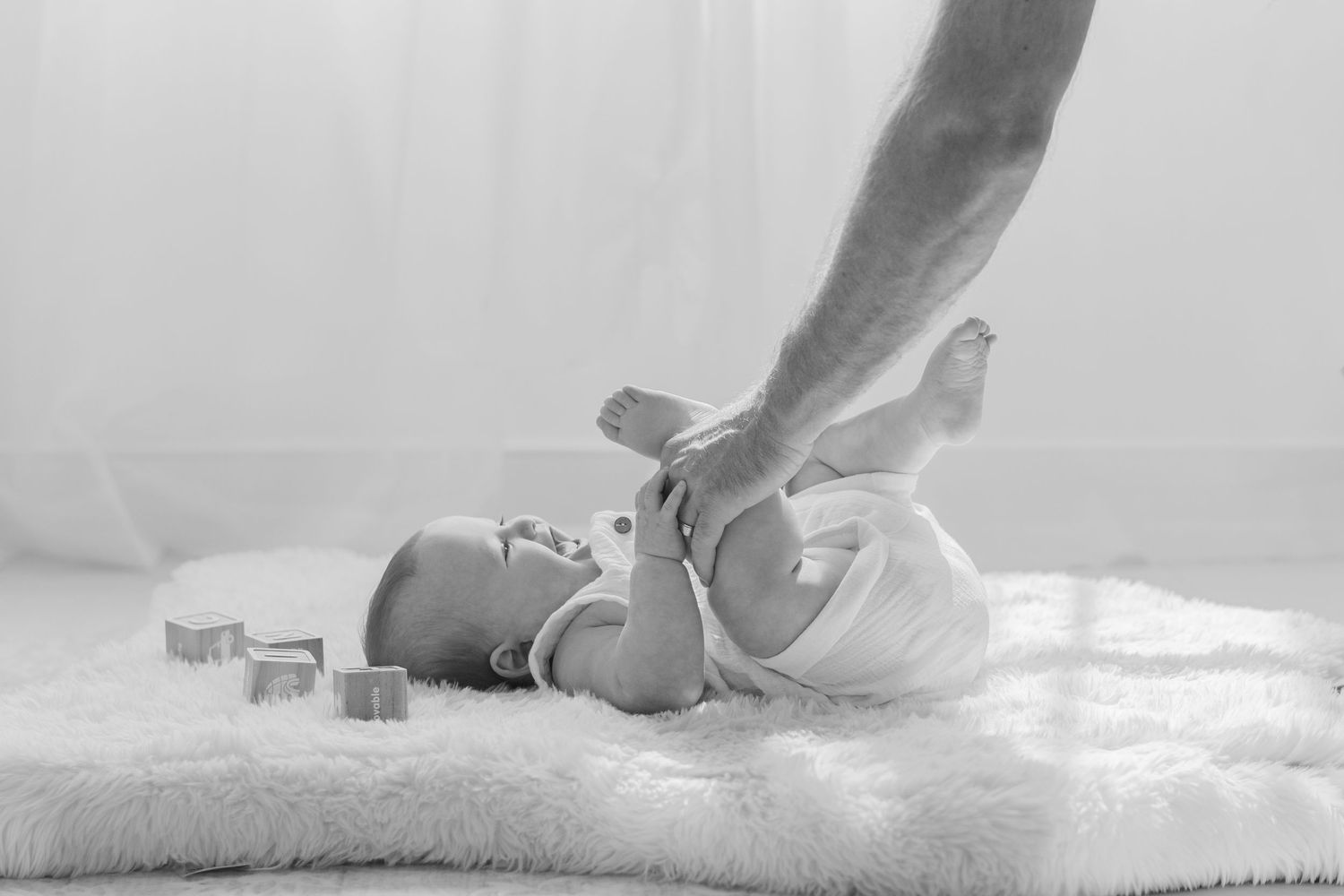 Black and white photo of a newborn baby lying on a fluffy rug while an adult gently holds its tiny feet.