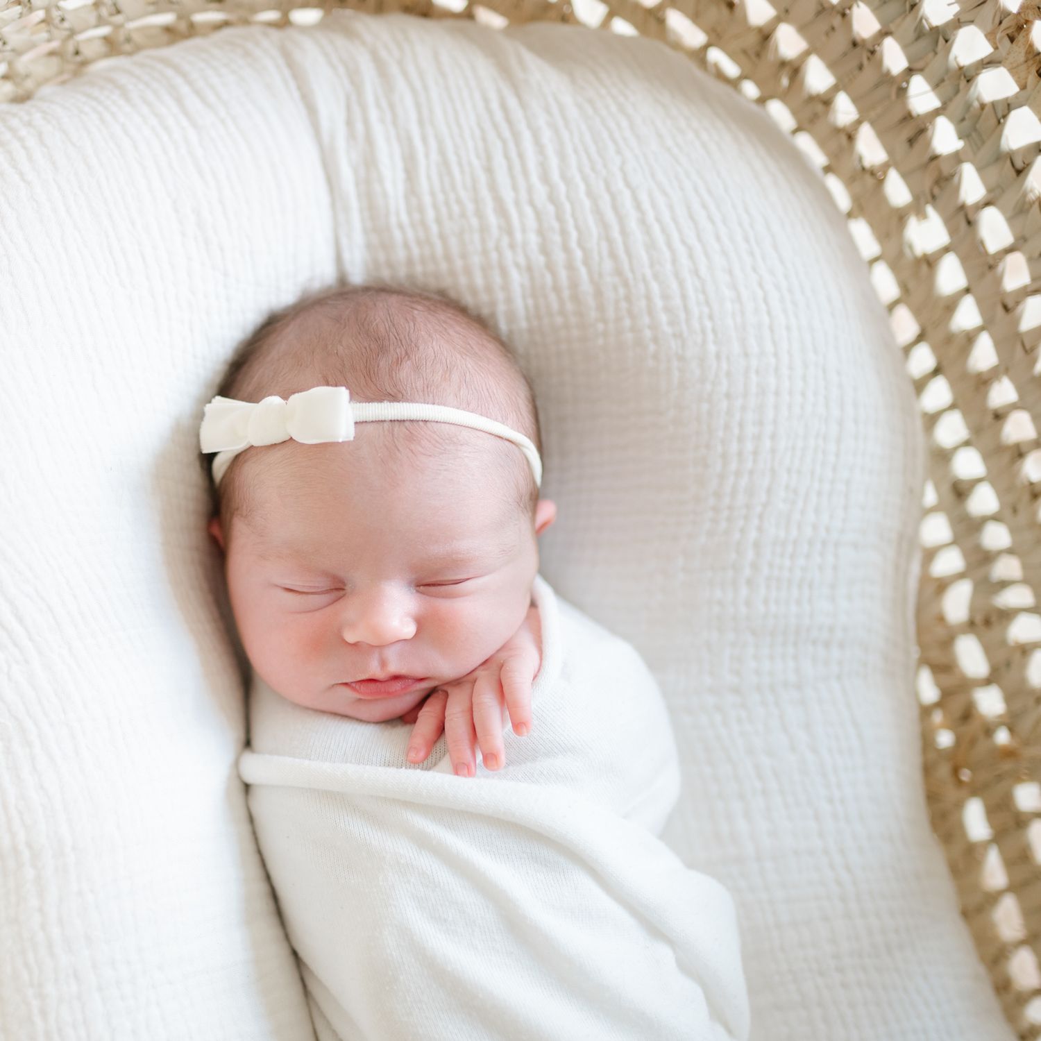 newborn baby in white swaddle and bow in Moses basket by Richmond newborn photographer