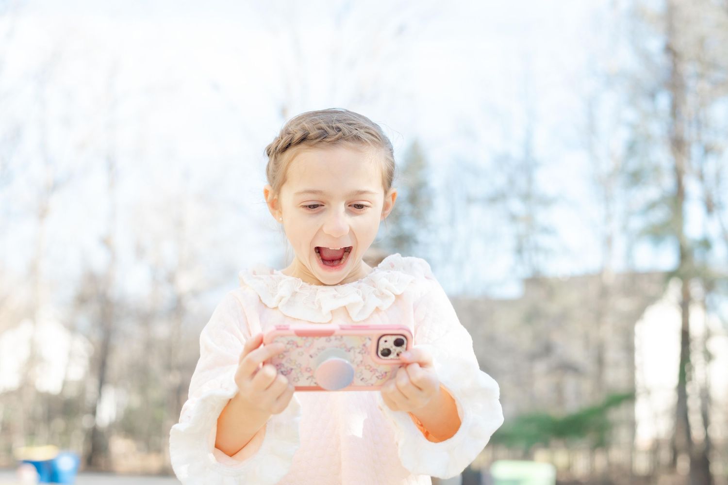 A child in a pink dress enjoys eating a sweet treat outdoors on a sunny winter day.
