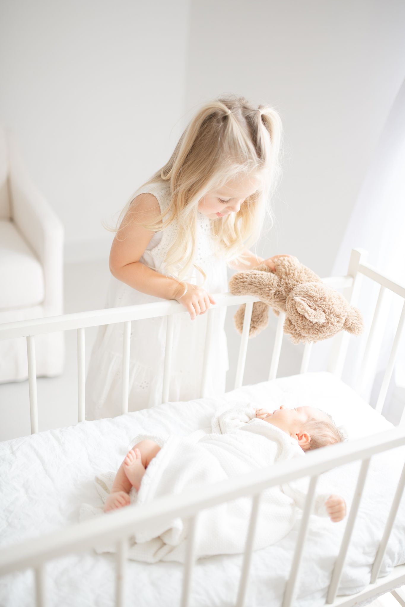 girl looking at new sister in crib in Richmond newborn photographer studio