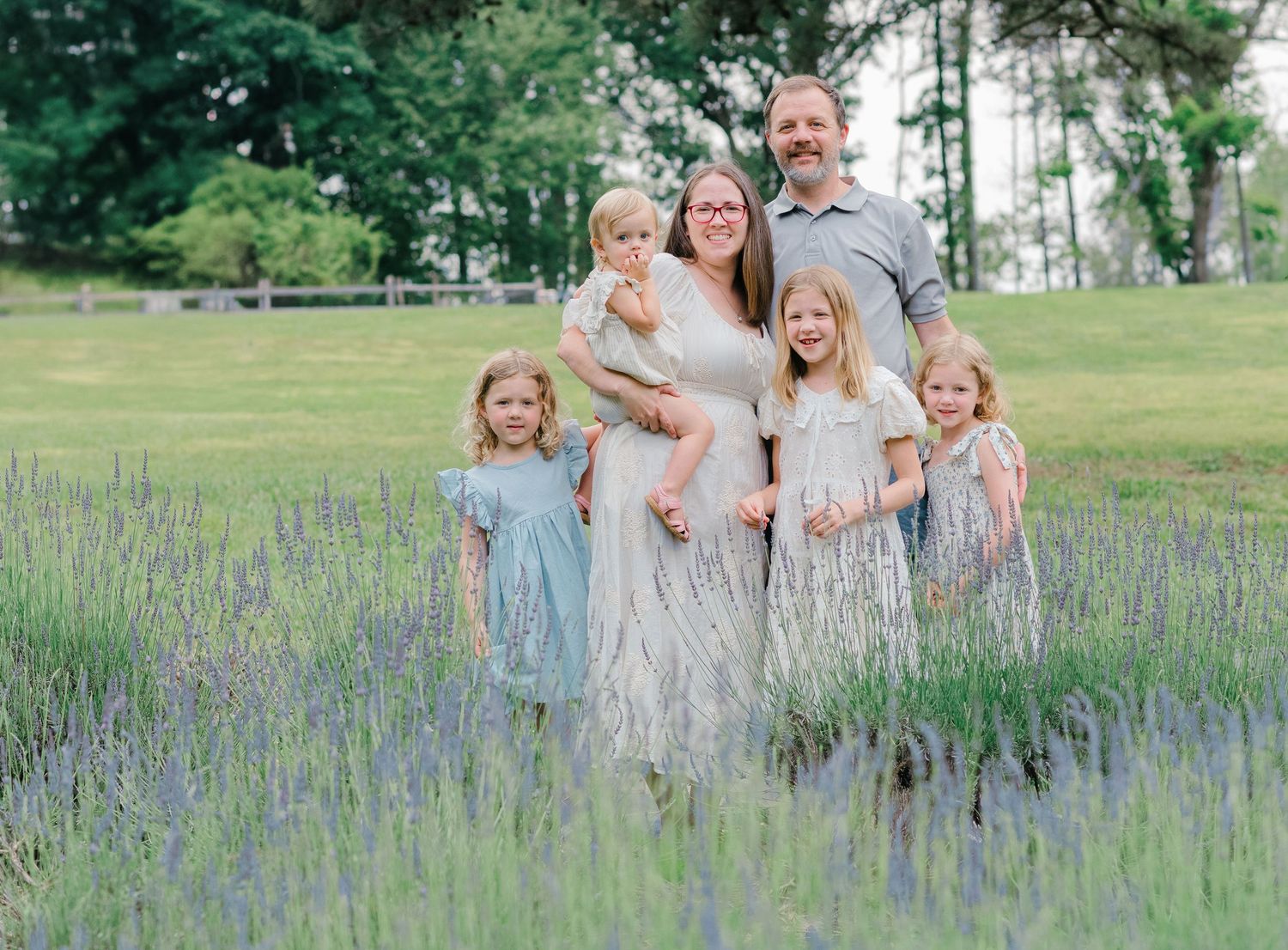 Family of six poses in lavender field, parents with four young daughters in matching dresses, outdoor portrait.