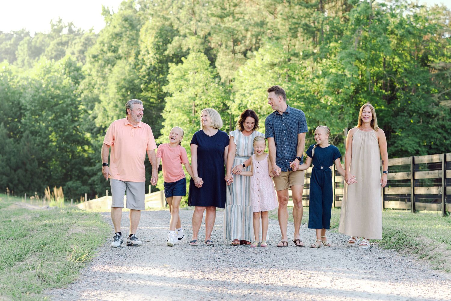Large family group walking together on a gravel path surrounded by lush green trees and a wooden fence.
