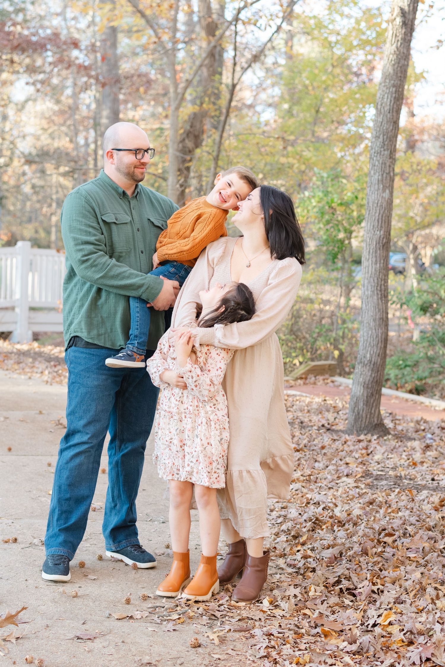 Family of four enjoying a fall outdoor photo session among autumn leaves and trees.