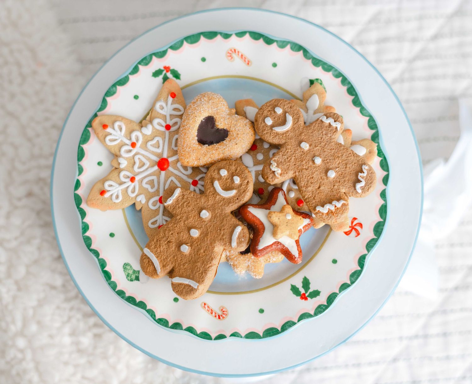 Assorted Christmas gingerbread cookies on a festive holly-decorated plate, including gingerbread men, snowflake, and star shapes.