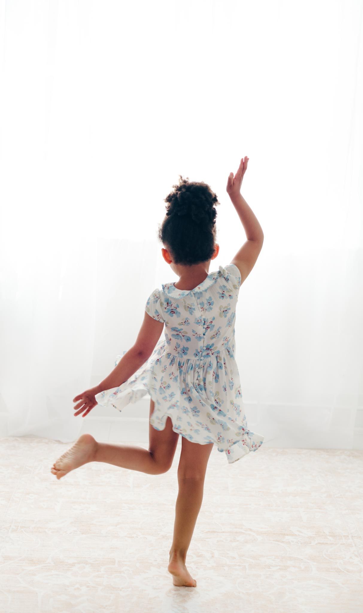 Person in blue floral dress dances and twirls on white floor.