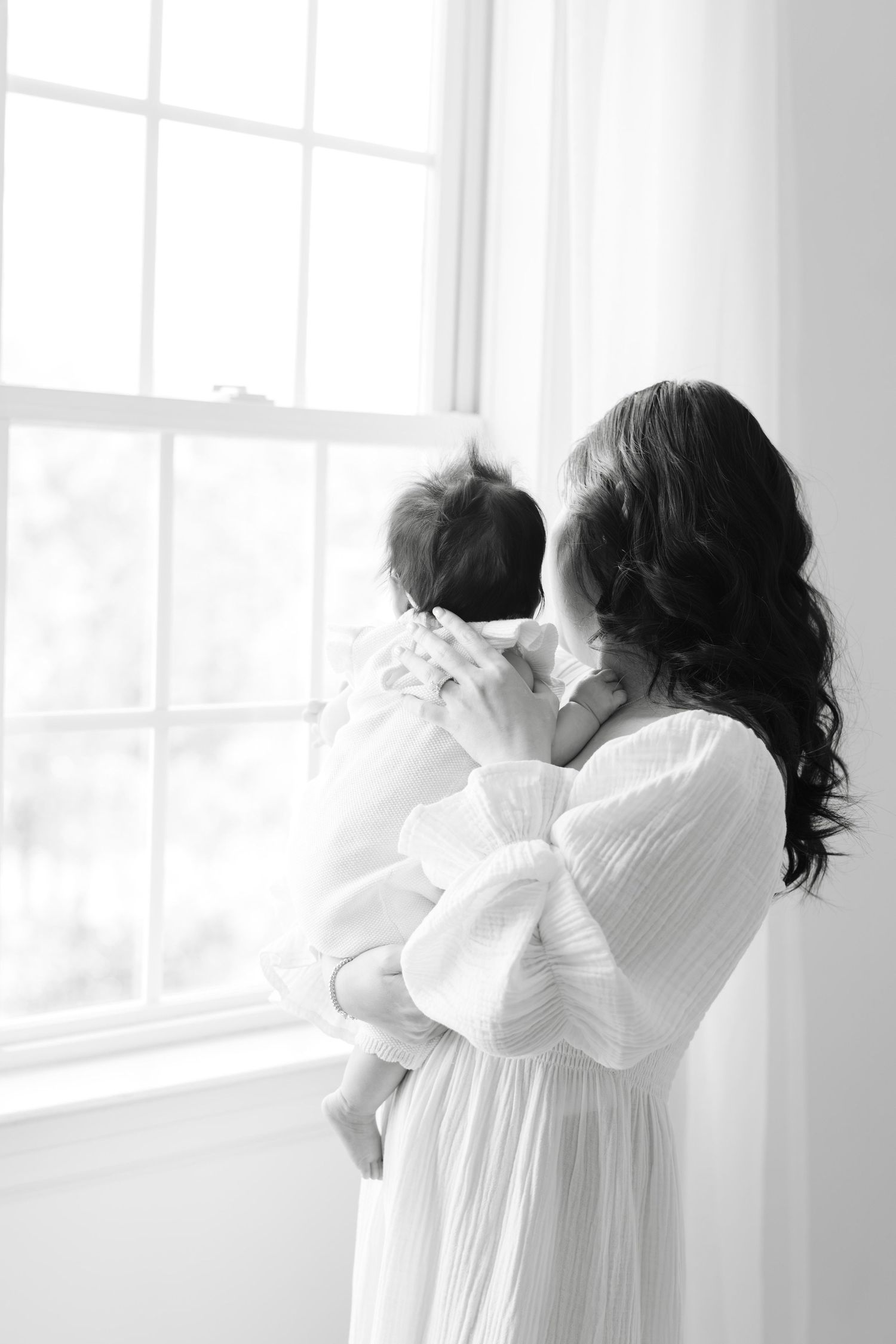 A series of four black and white photos showing a tender moment between two people in white clothing by a window.