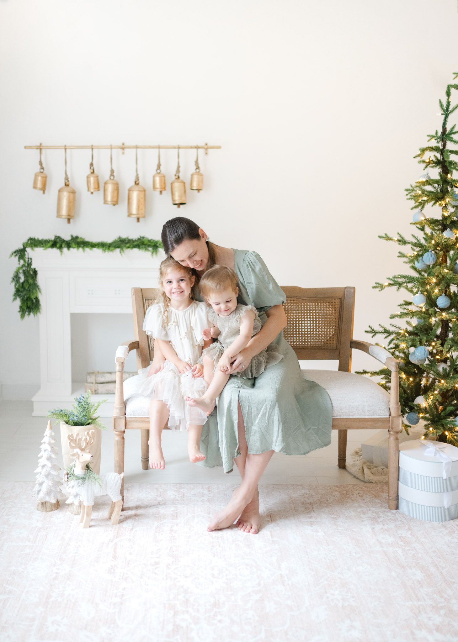 Minimalist holiday scene with family sitting on a cane bench near a decorated Christmas tree in an all-white room.