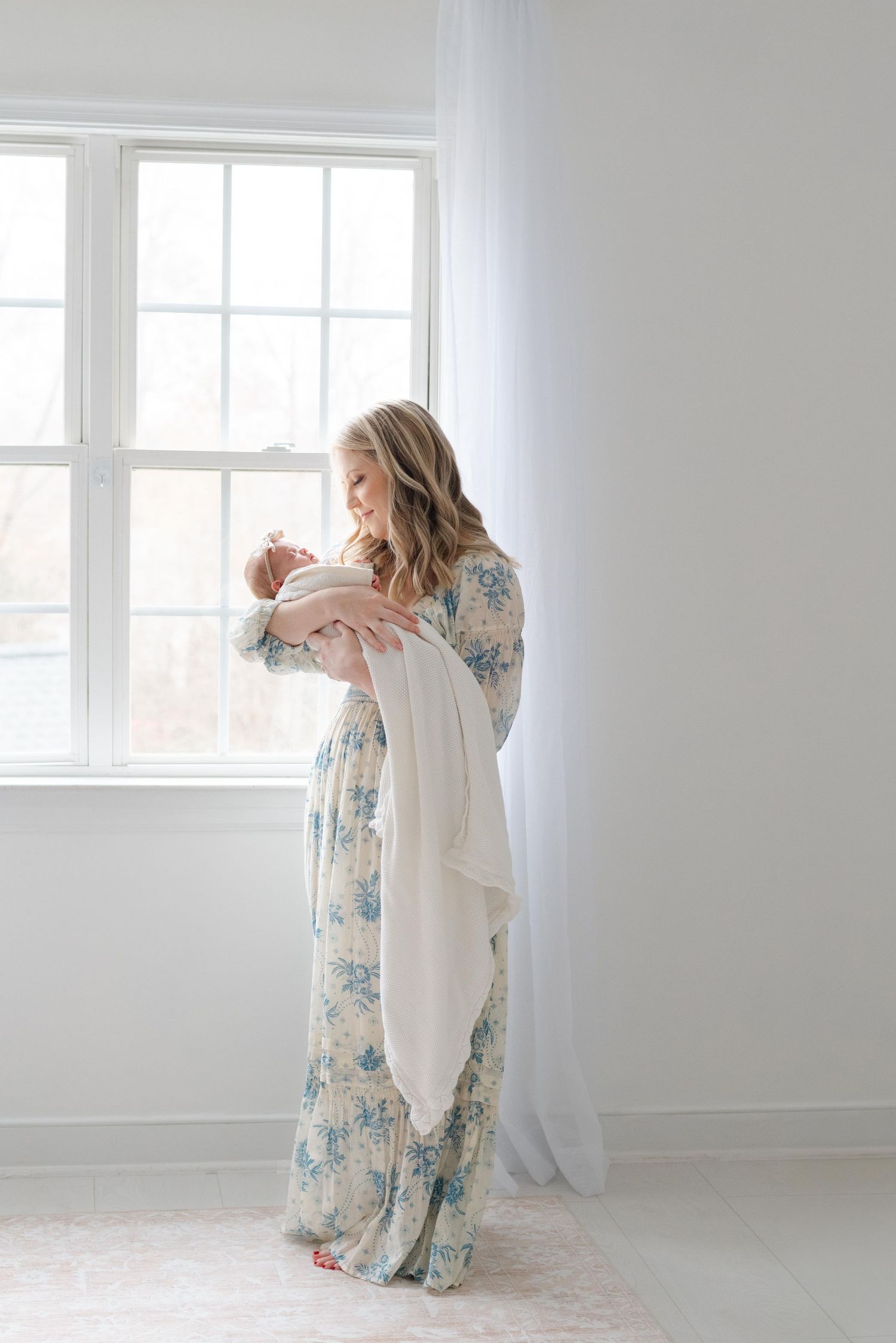 Mother holding newborn by window in soft natural light studio, Midlothian newborn photography