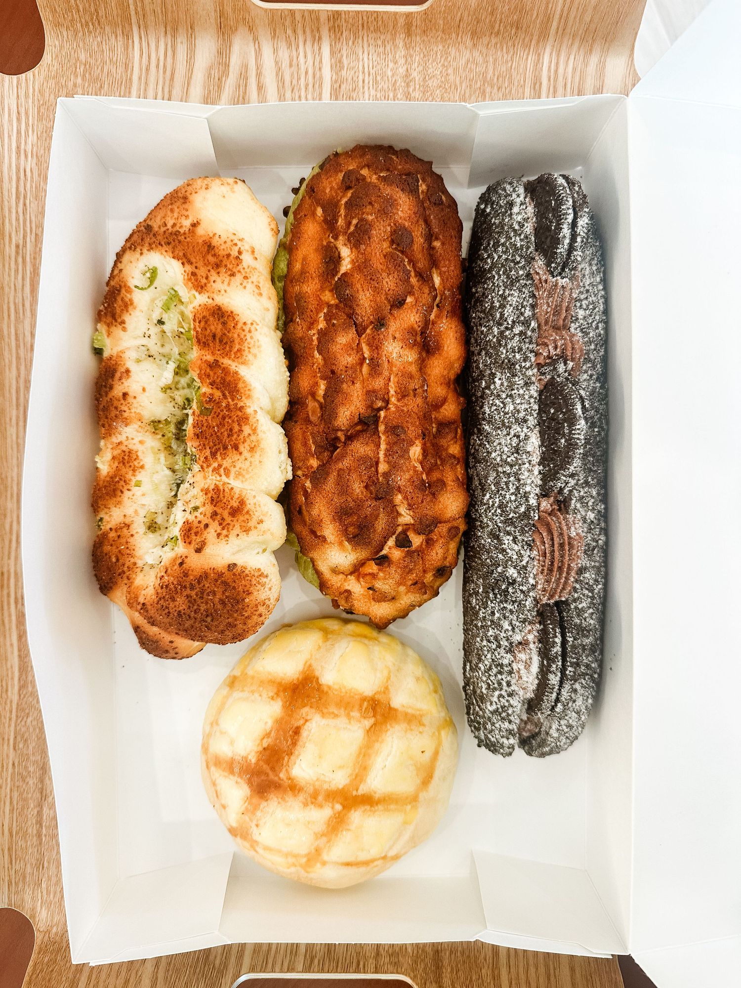 Assorted baked goods including bread rolls and dark pastries arranged on white paper.