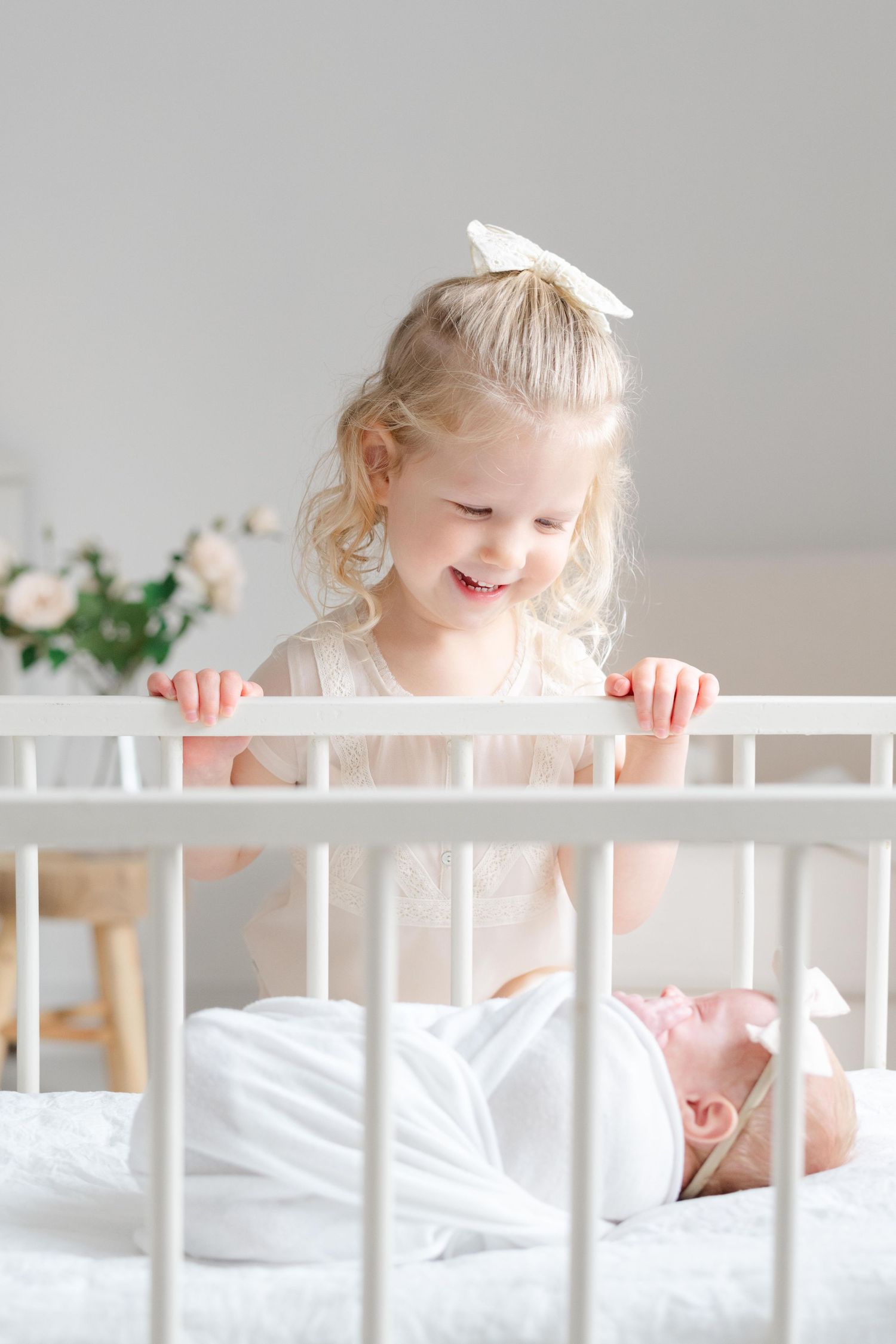 Toddler looking into crib at newborn sibling in bright white studio, Richmond newborn photography