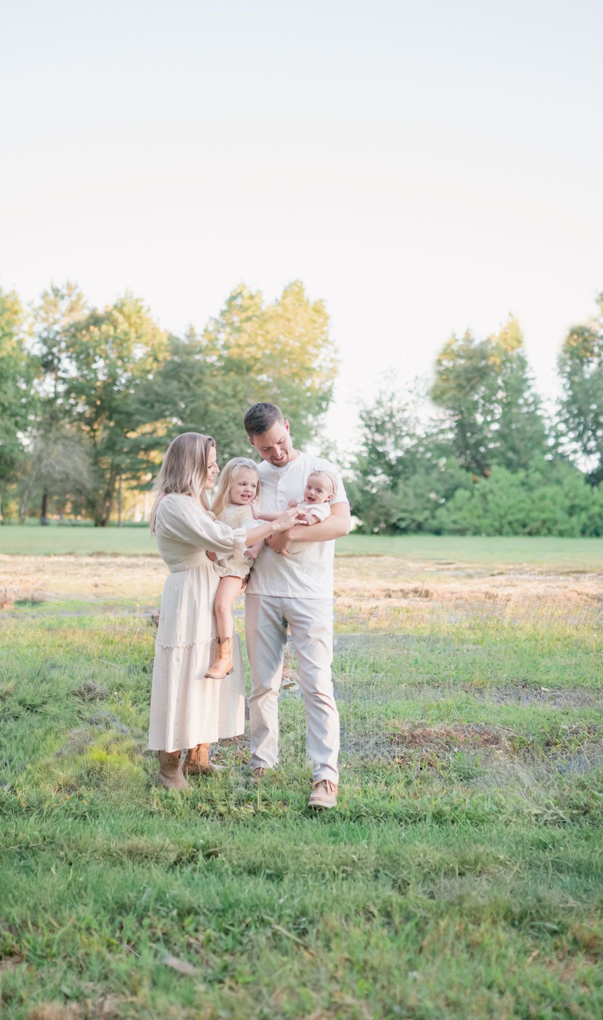Family wearing neutral colors walking together in a sunlit meadow during golden hour.