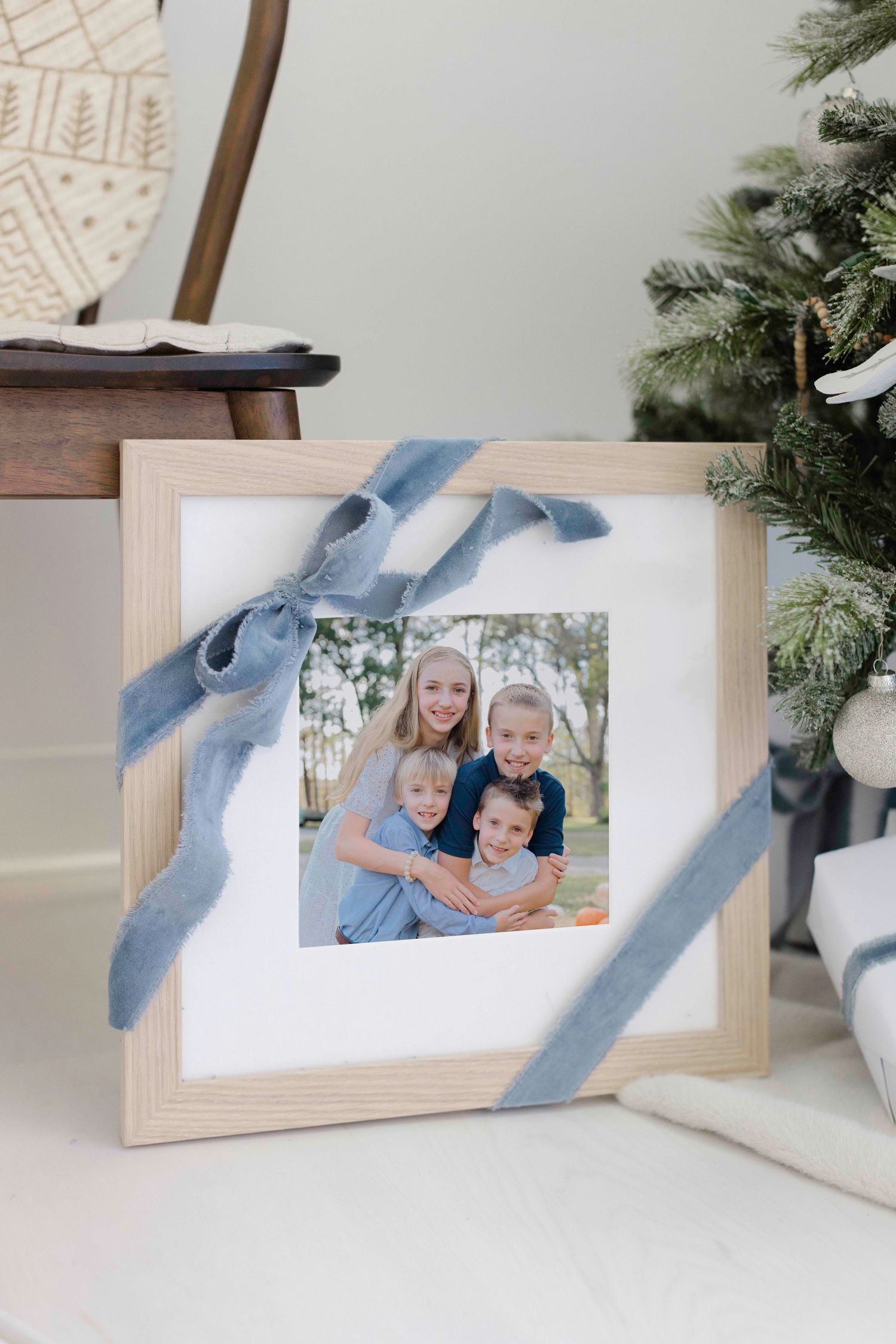 A wooden picture frame decorated with a blue velvet ribbon sits near evergreen branches and holiday decor.