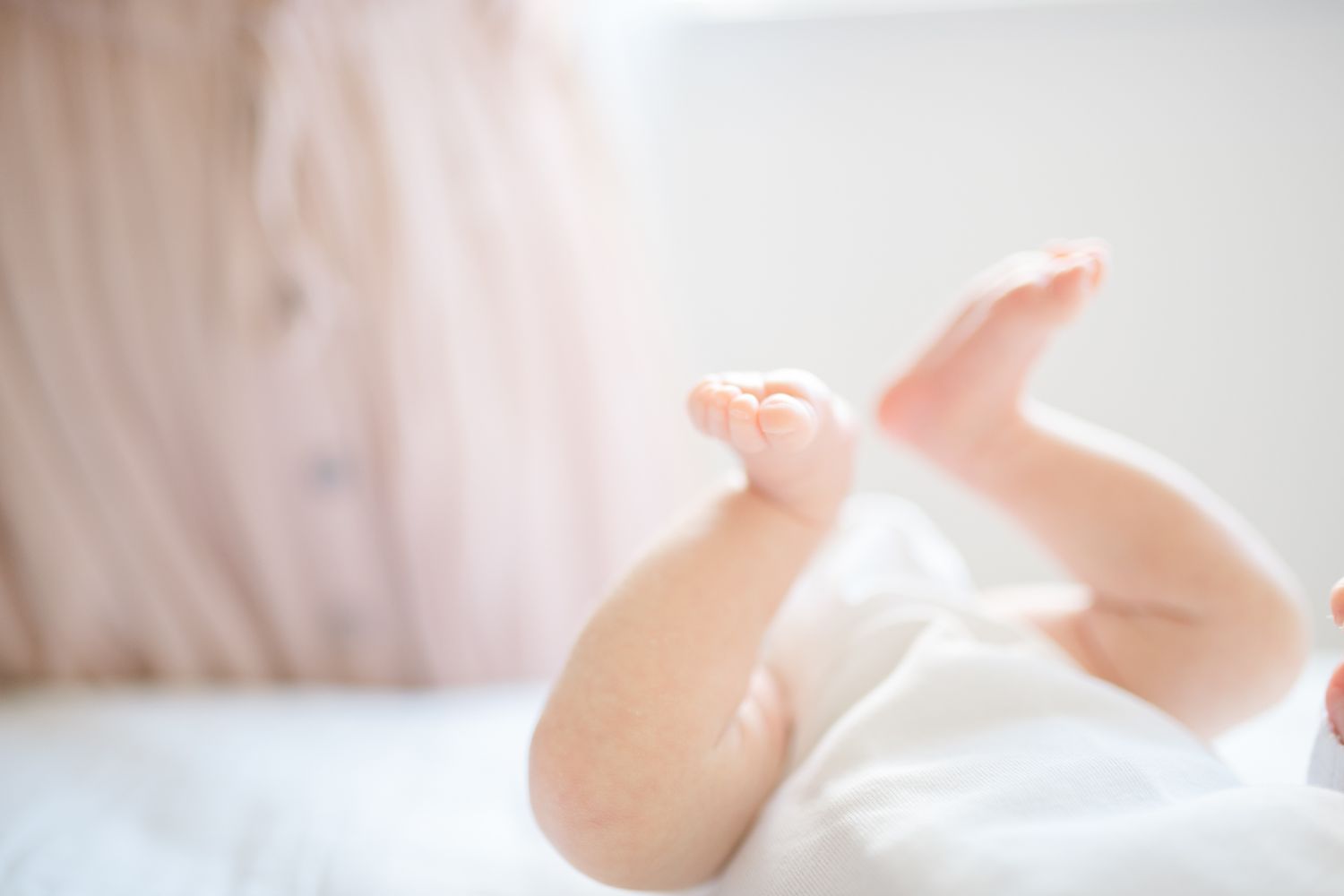 Soft focus close-up of baby feet against white bedding.