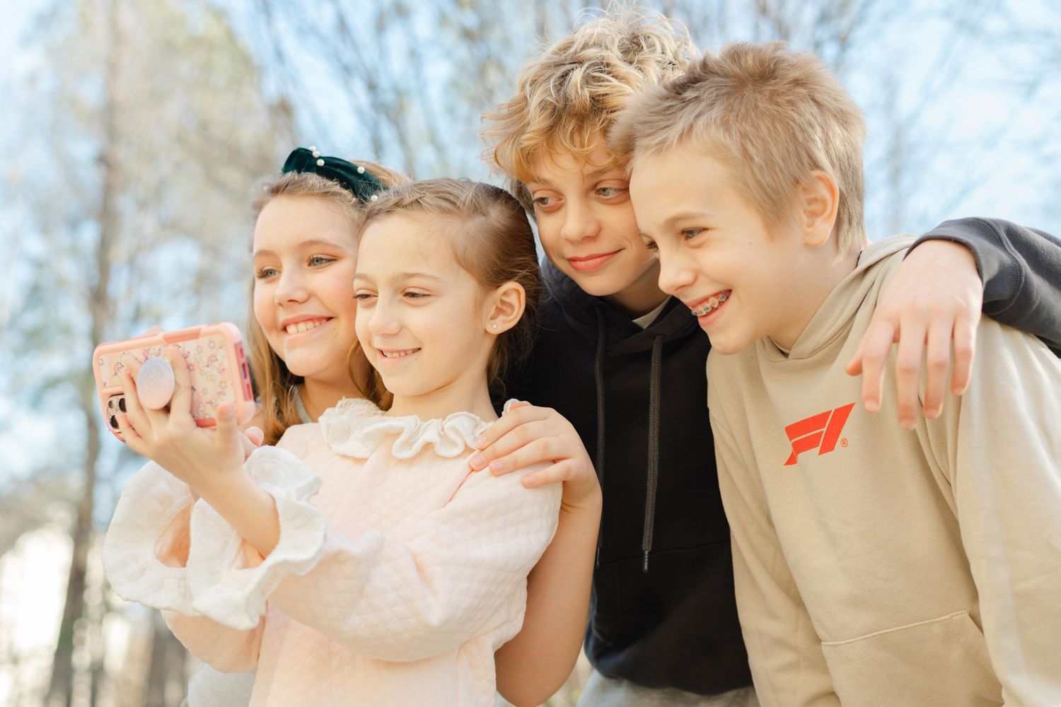 A group of friends huddle together and smile outdoors on a bright sunny day.