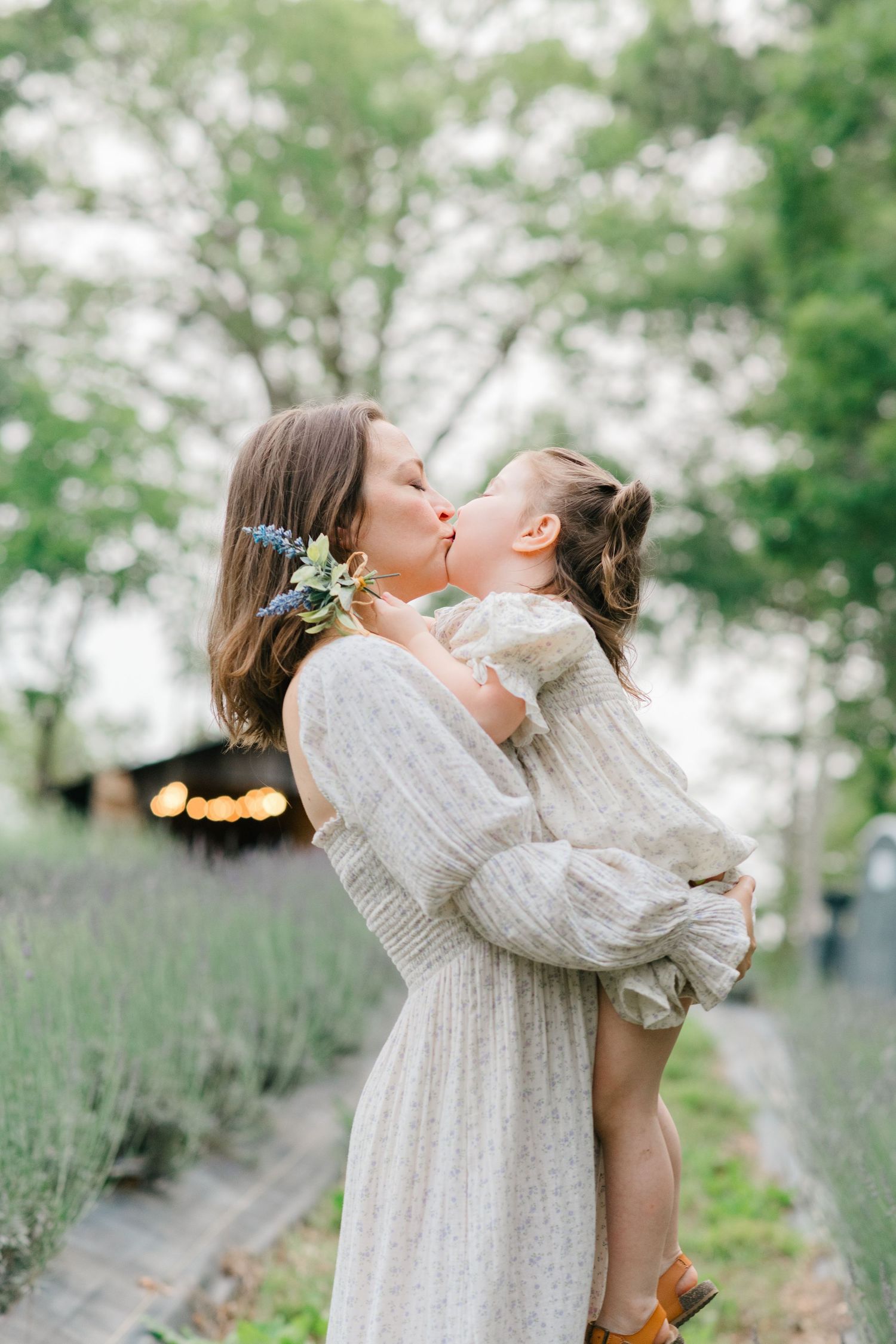 A mother and daughter in matching white dresses share tender moments in a garden setting with bokeh lights.