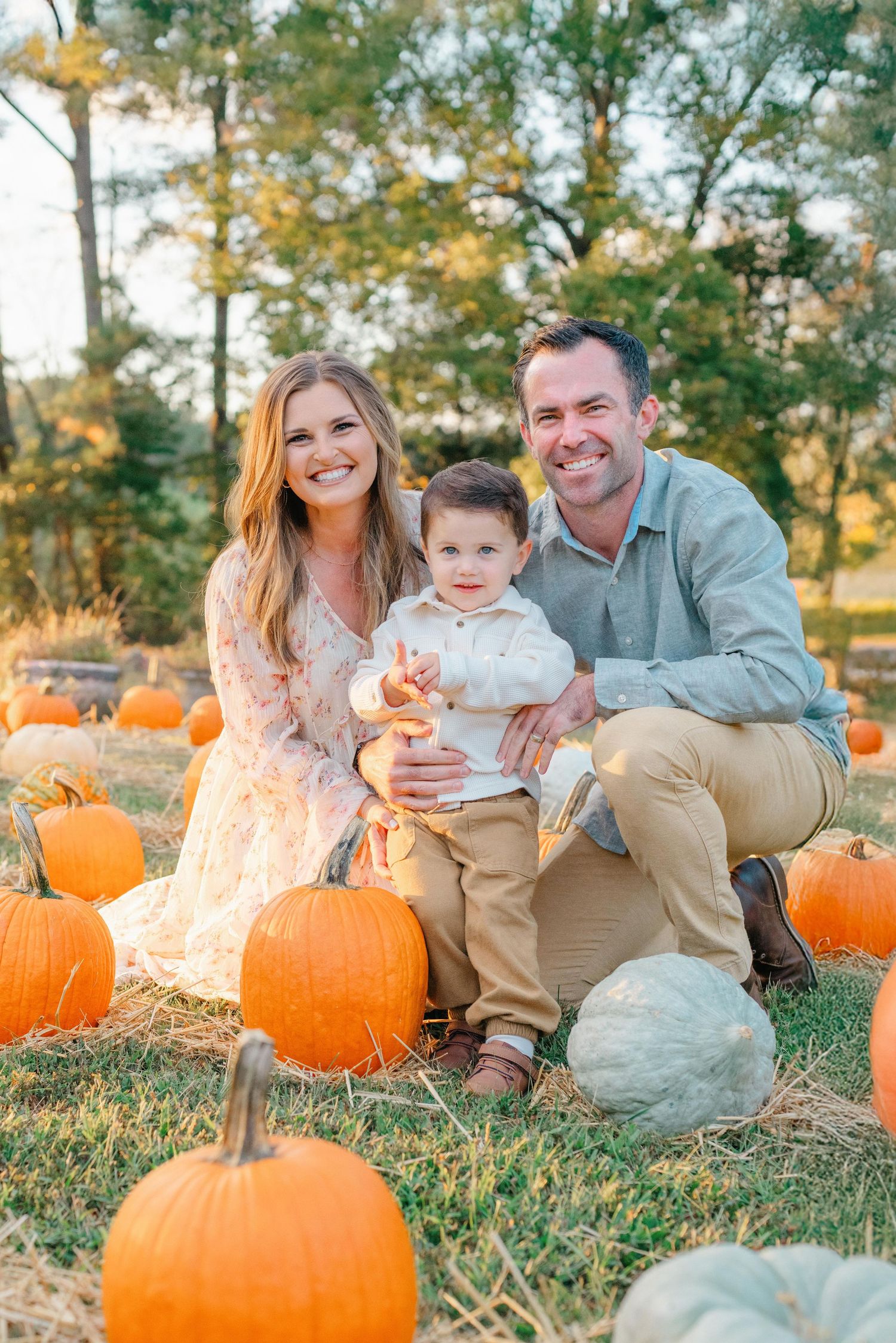 Family enjoying autumn day at pumpkin patch with hay bales and orange pumpkins during golden hour.