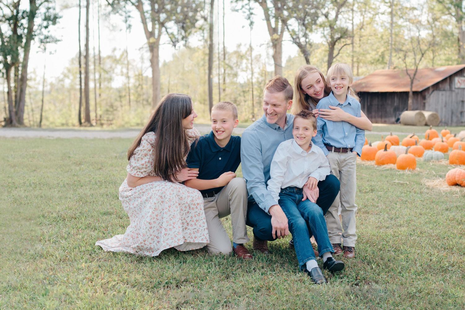 Family group sitting together in outdoor field during fall season.